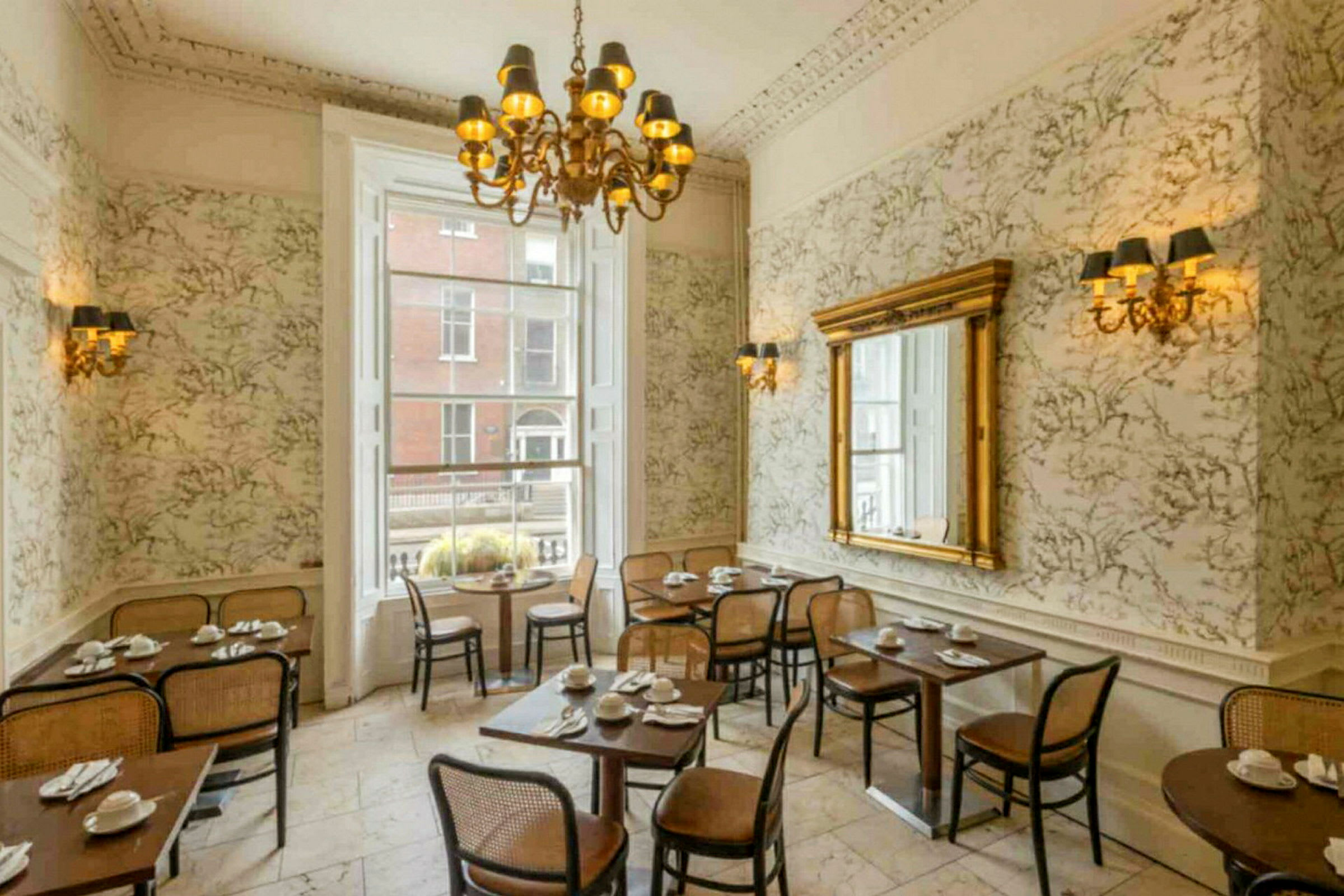 En restaurantinteriør med klassisk innredning, bord og stoler, stor speil og en lysekrone. (AI-generert tekst)
