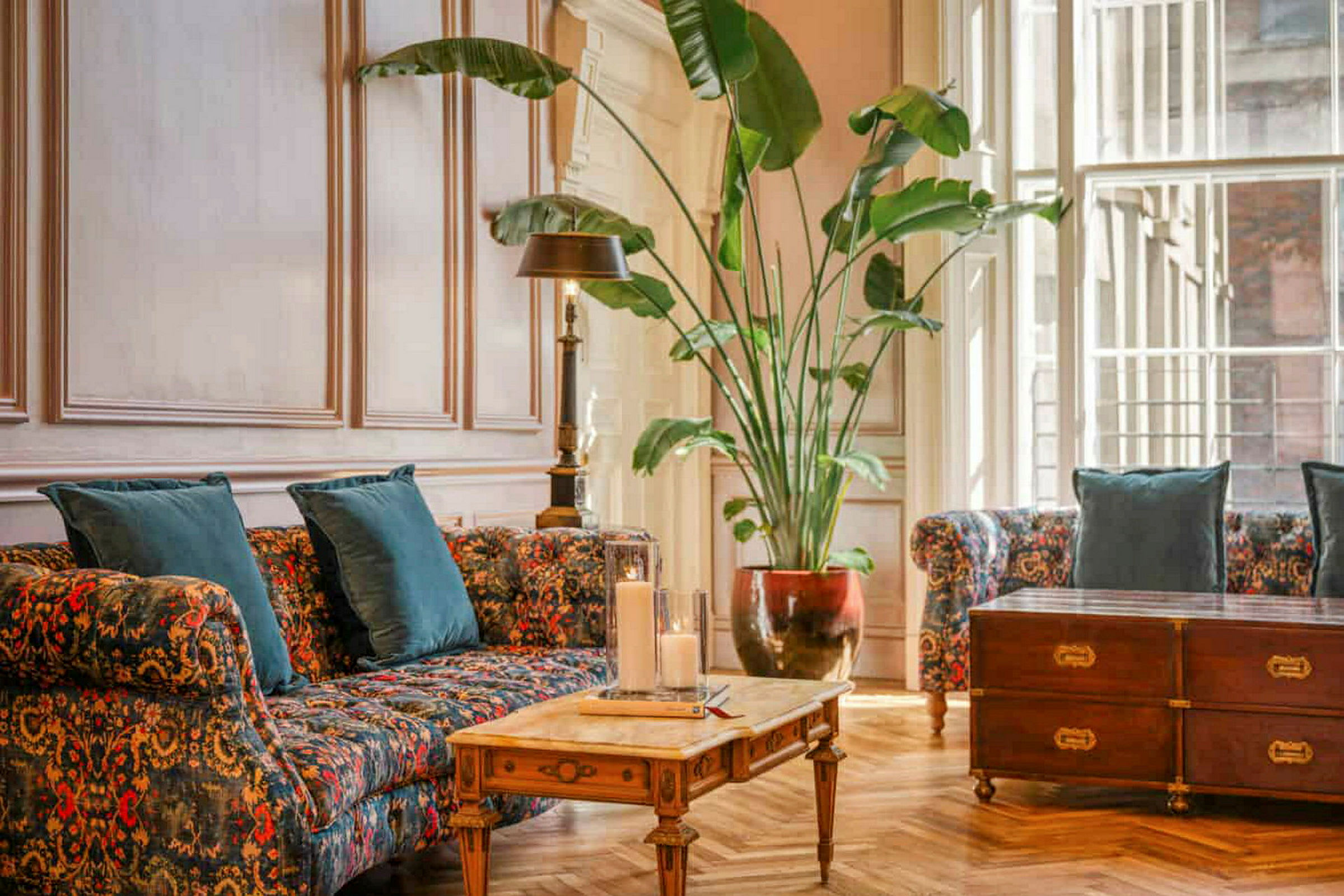 En stue med blomstrede sofaer, et trebord og en stor grønn potteplante. (AI-generert tekst)