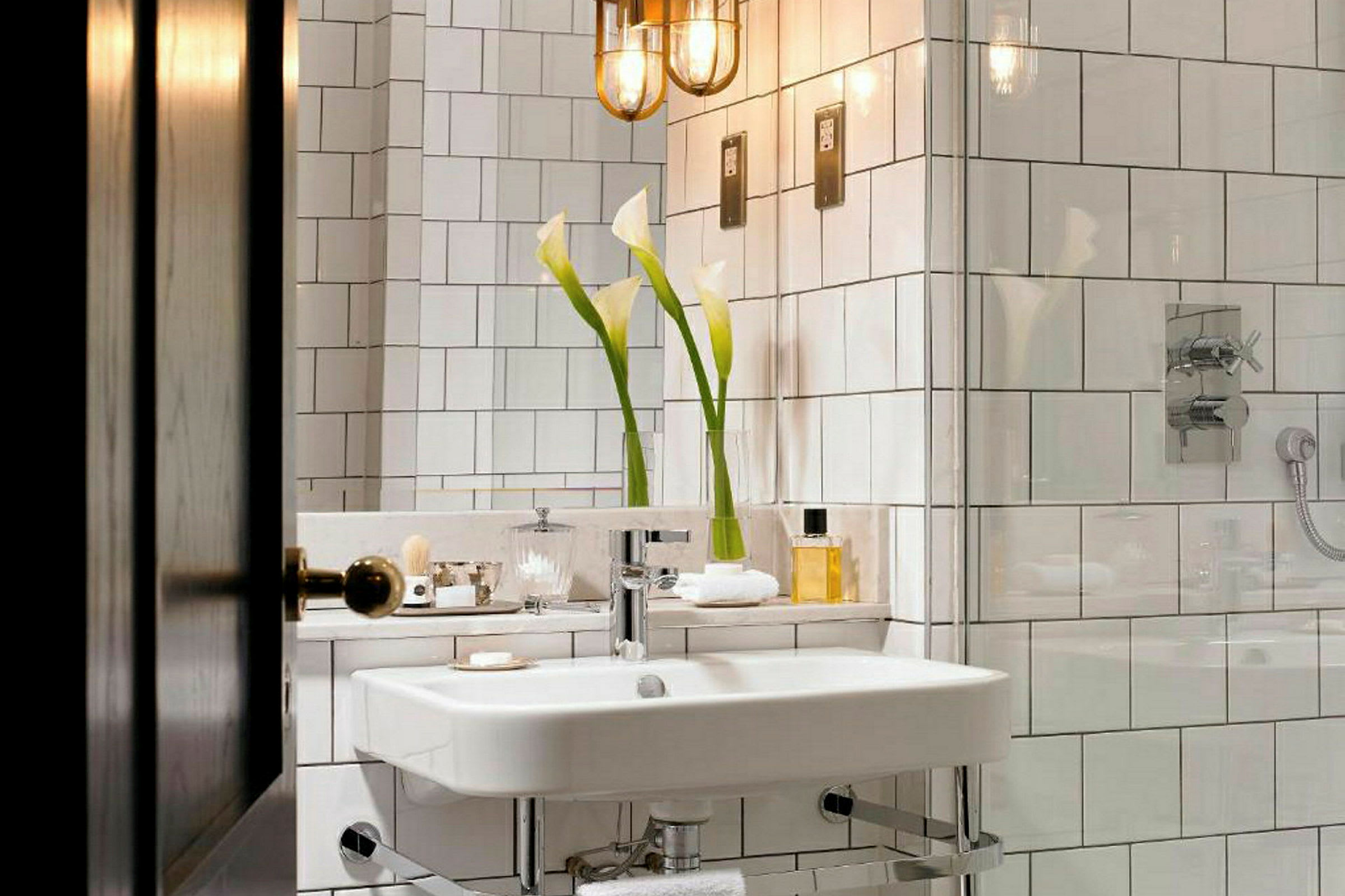 Et baderom med hvite flisvegger, en vask og speil, dekorert med hvite blomster og en glassdusj. (AI-generert tekst)
