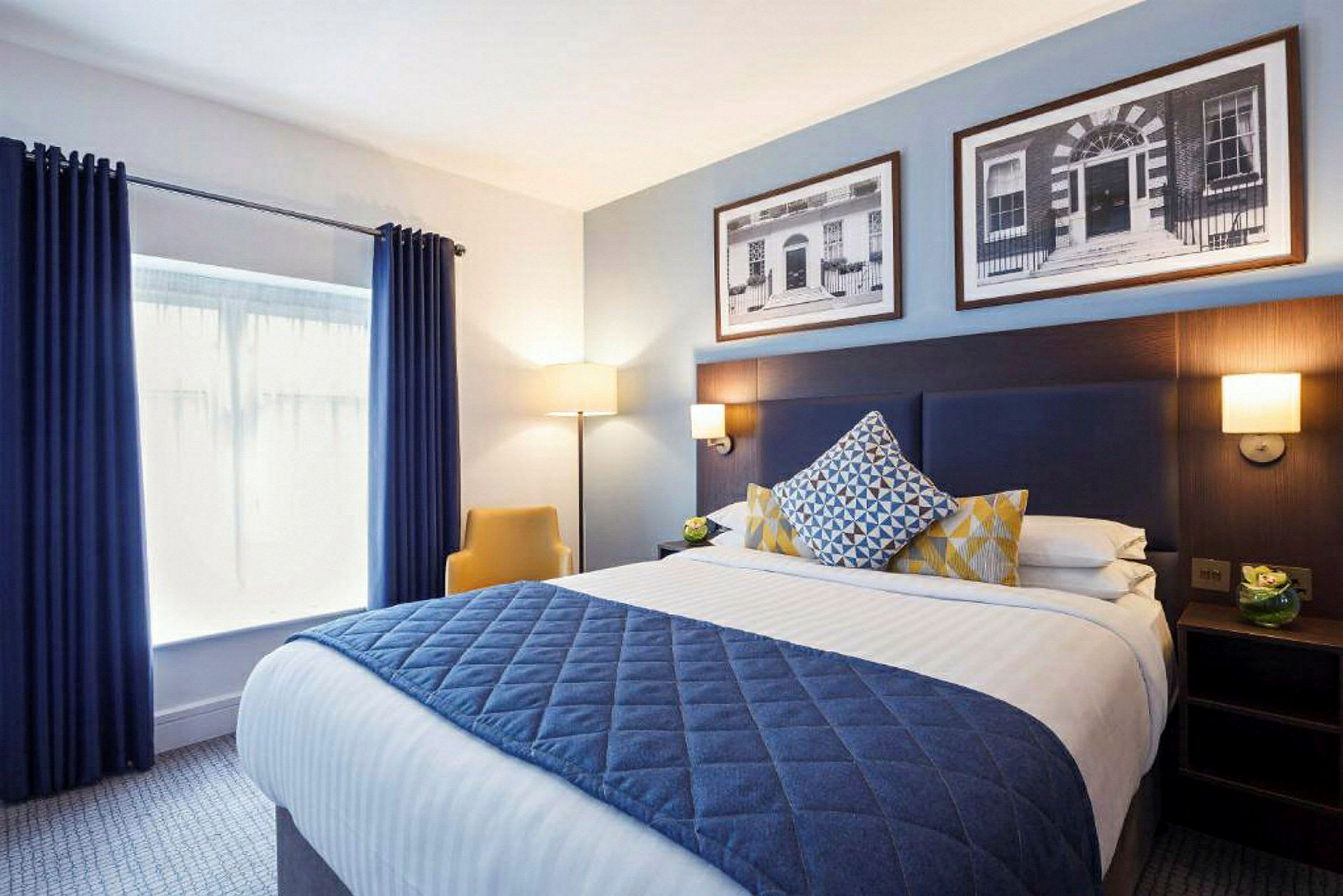 Moderne innredet hotellrom med en dobbeltseng, dekorerte puter og et teppe i blå nyanse. (AI-generert tekst)