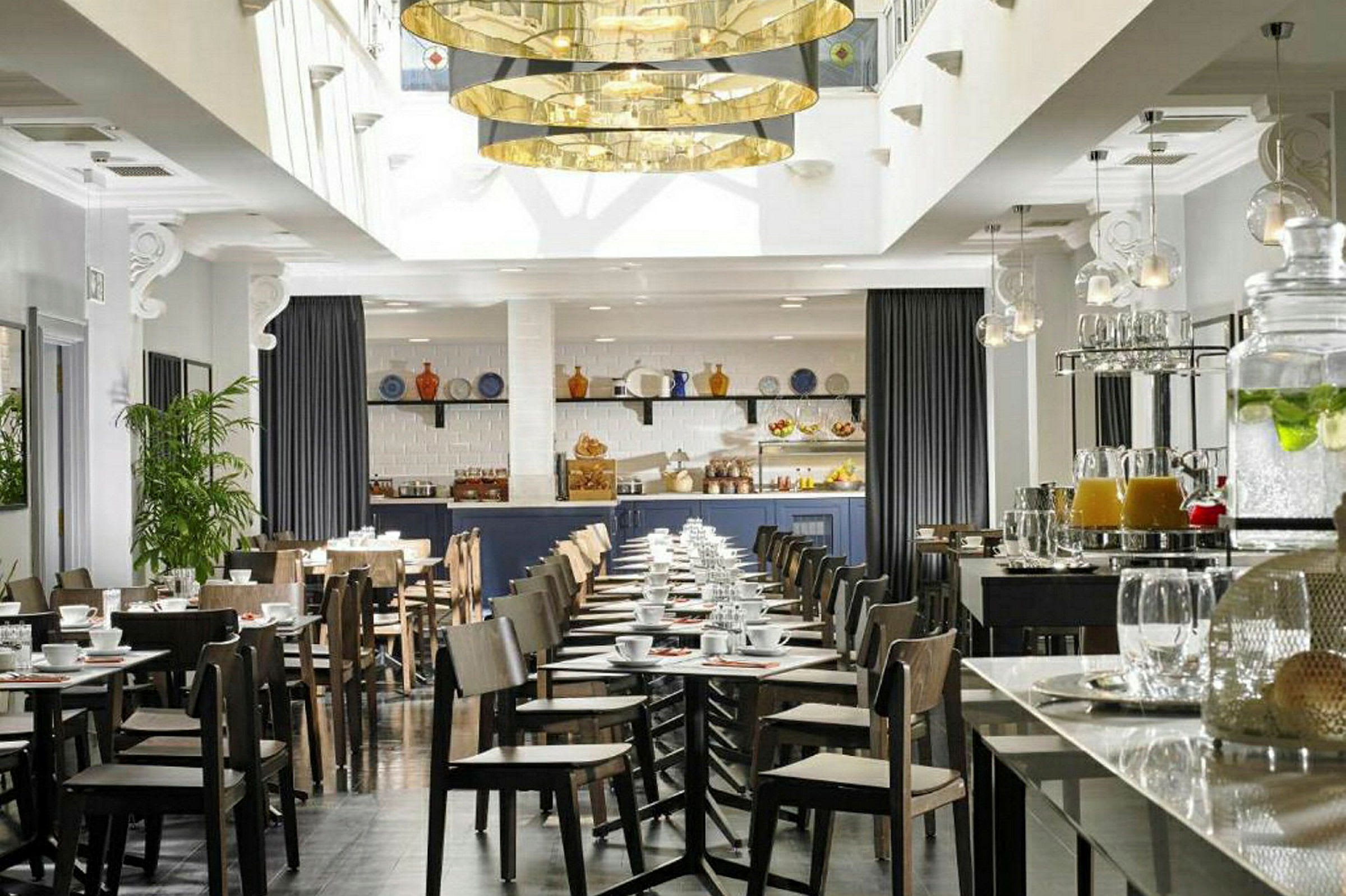 En moderne innredet kafé eller restaurant med bord og stoler, en serveringsdisk og dekorasjoner som planter og hengende lamper. (AI-generert tekst)