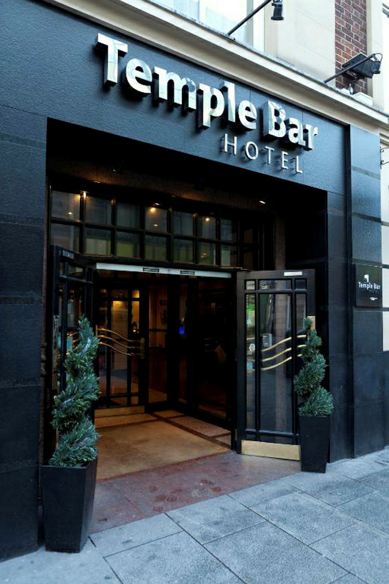 Inngangen til Temple Bar Hotel med skilt over og to potteplanter på hver side av døren. (AI-generert tekst)