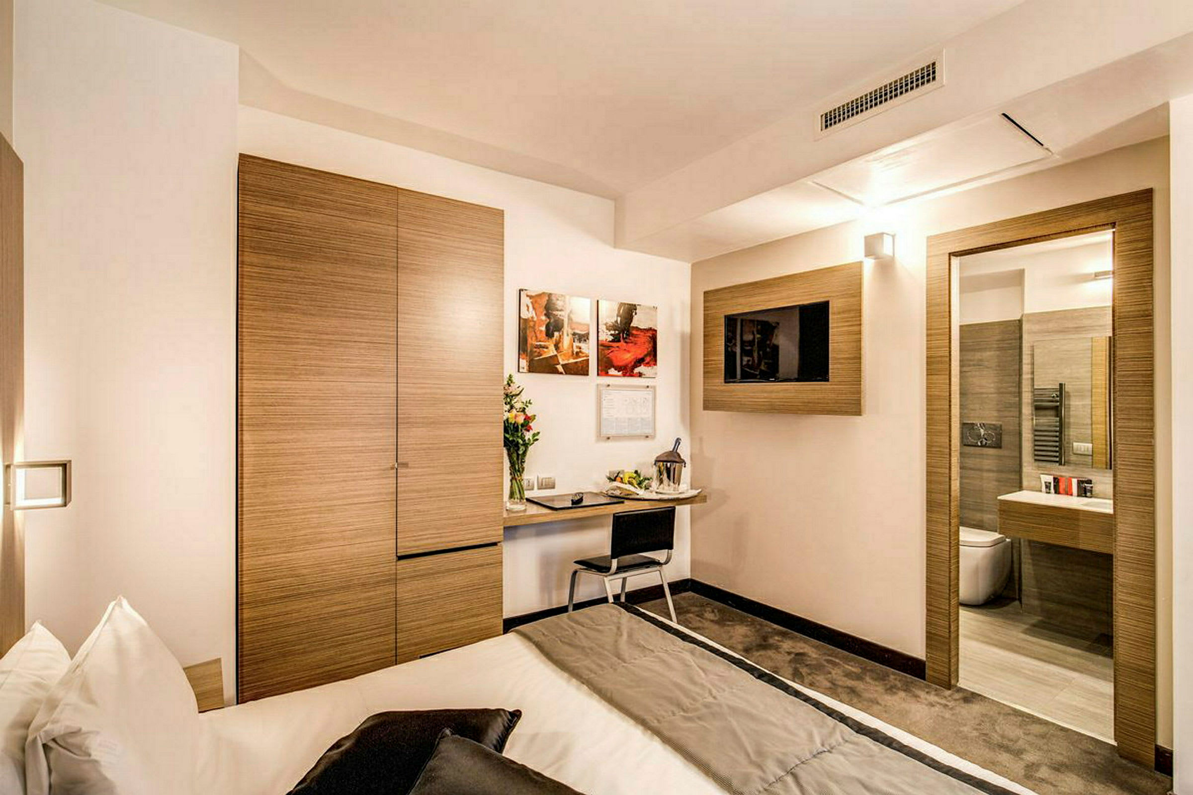 Et moderne hotellrom med et skrivebord, en seng og en TV på veggen. (AI-generert tekst)