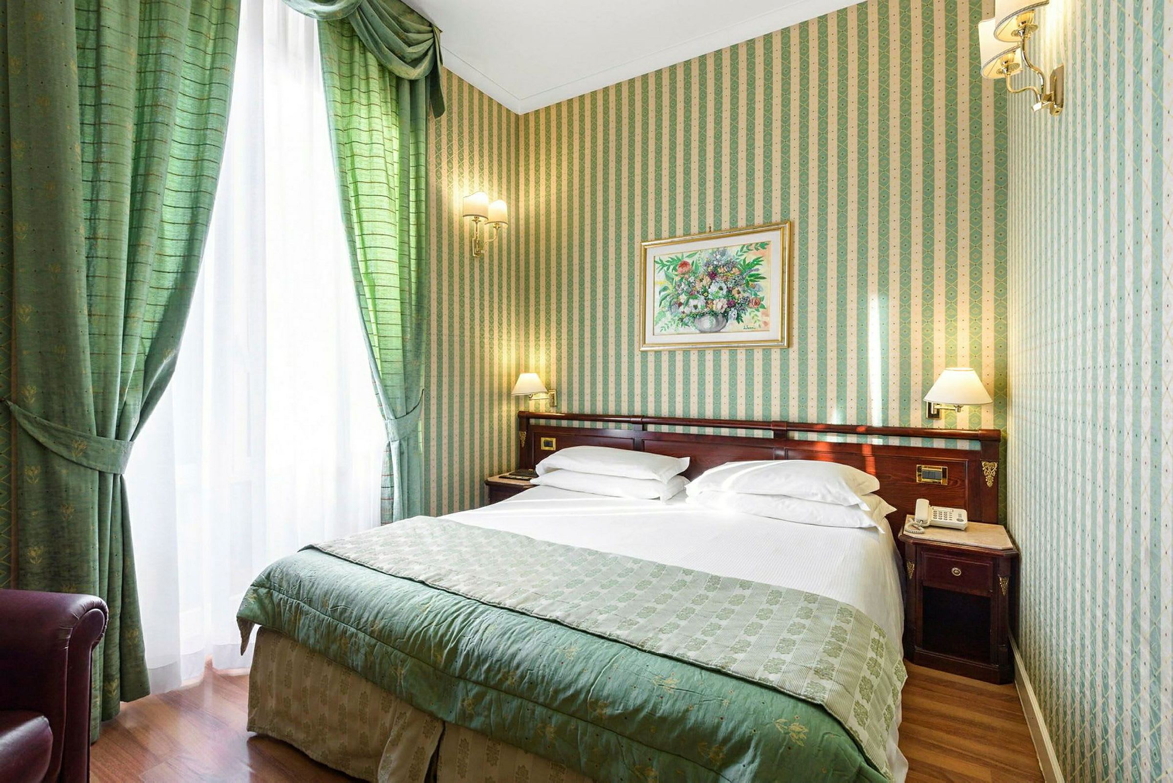 Hotellrom med to senger, grønne gardiner og stripete tapet i grønne og beige toner. Et bilde med blomstermotiv er plassert over sengegavlen. (AI-generert tekst)