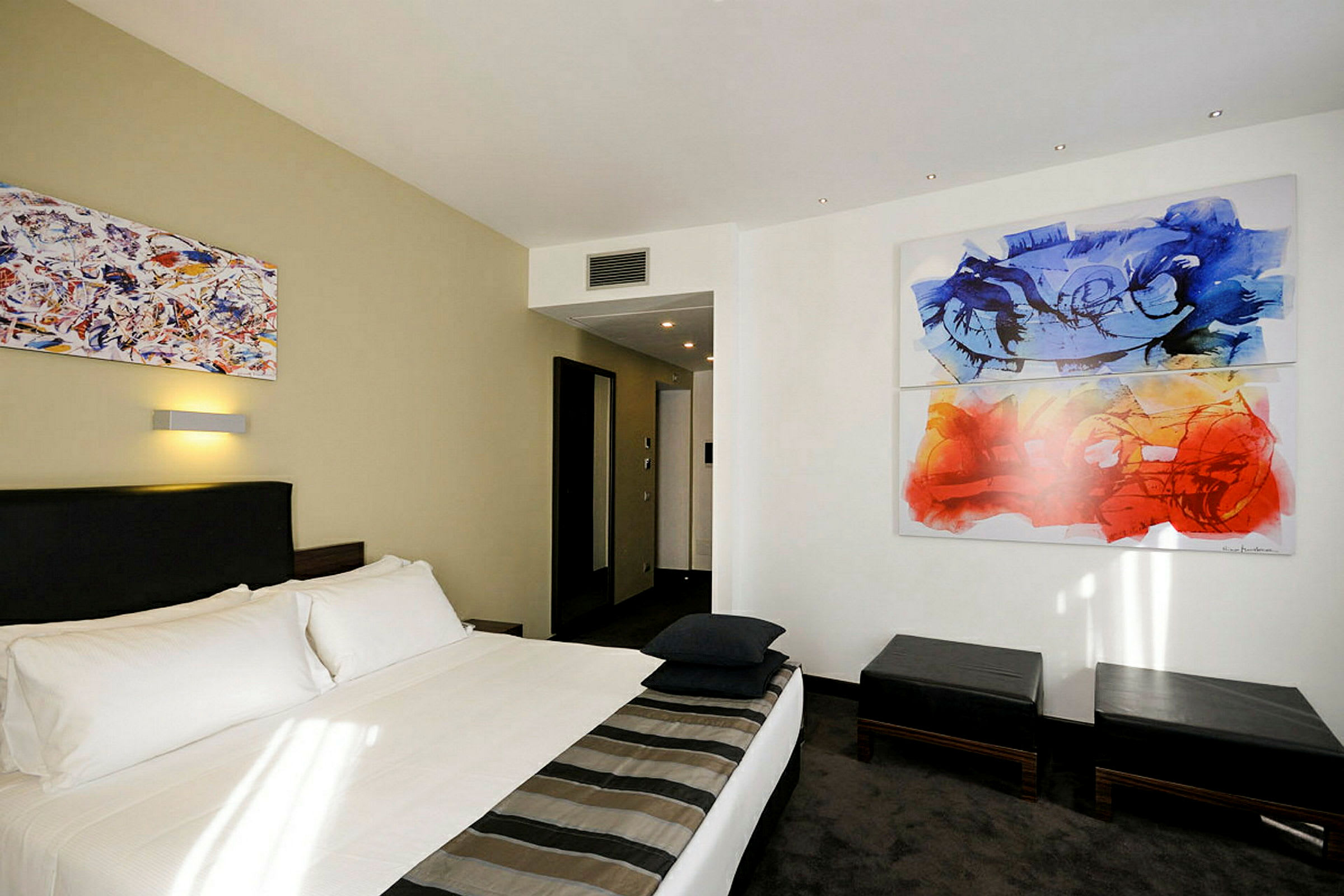 Hotellrom med en dobbeltseng og abstrakt kunst på veggen. (AI-generert tekst)
