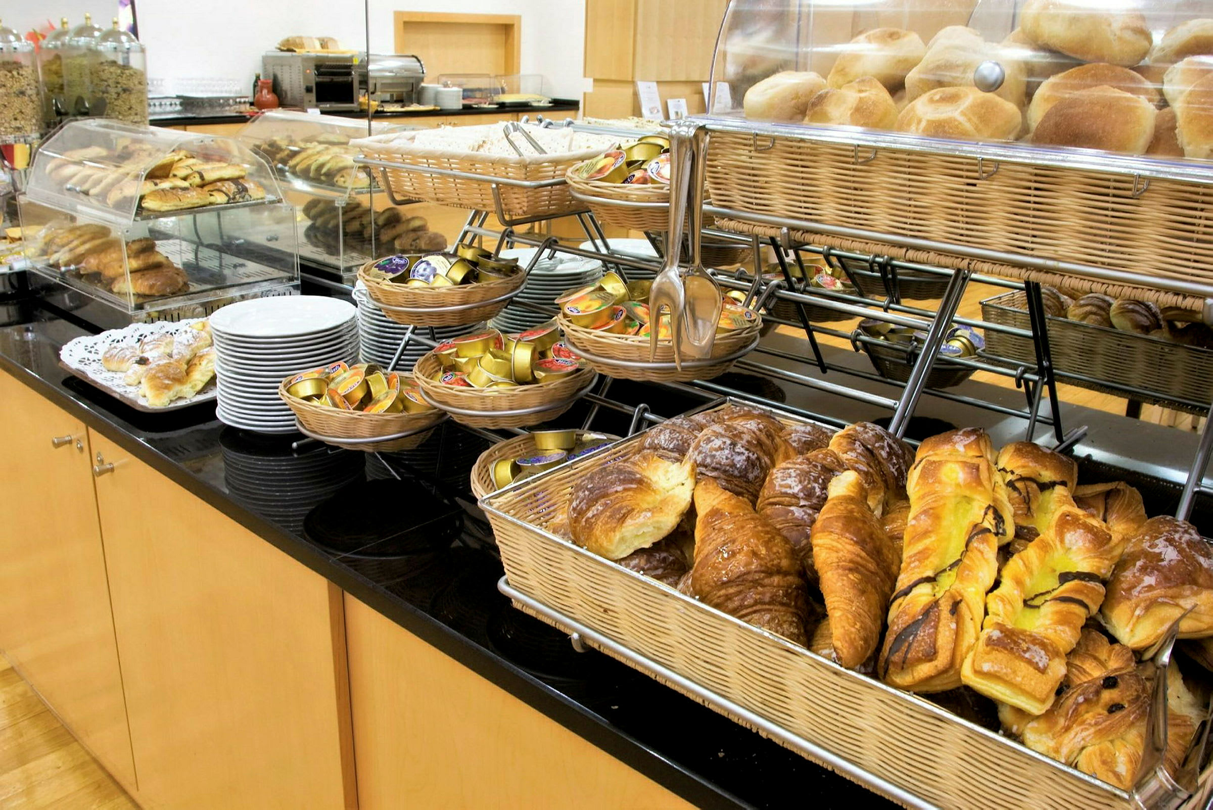 Et frokostbuffébord med ulike typer bakverk, brød i kurver og porsjoner med syltetøy. (AI-generert tekst)