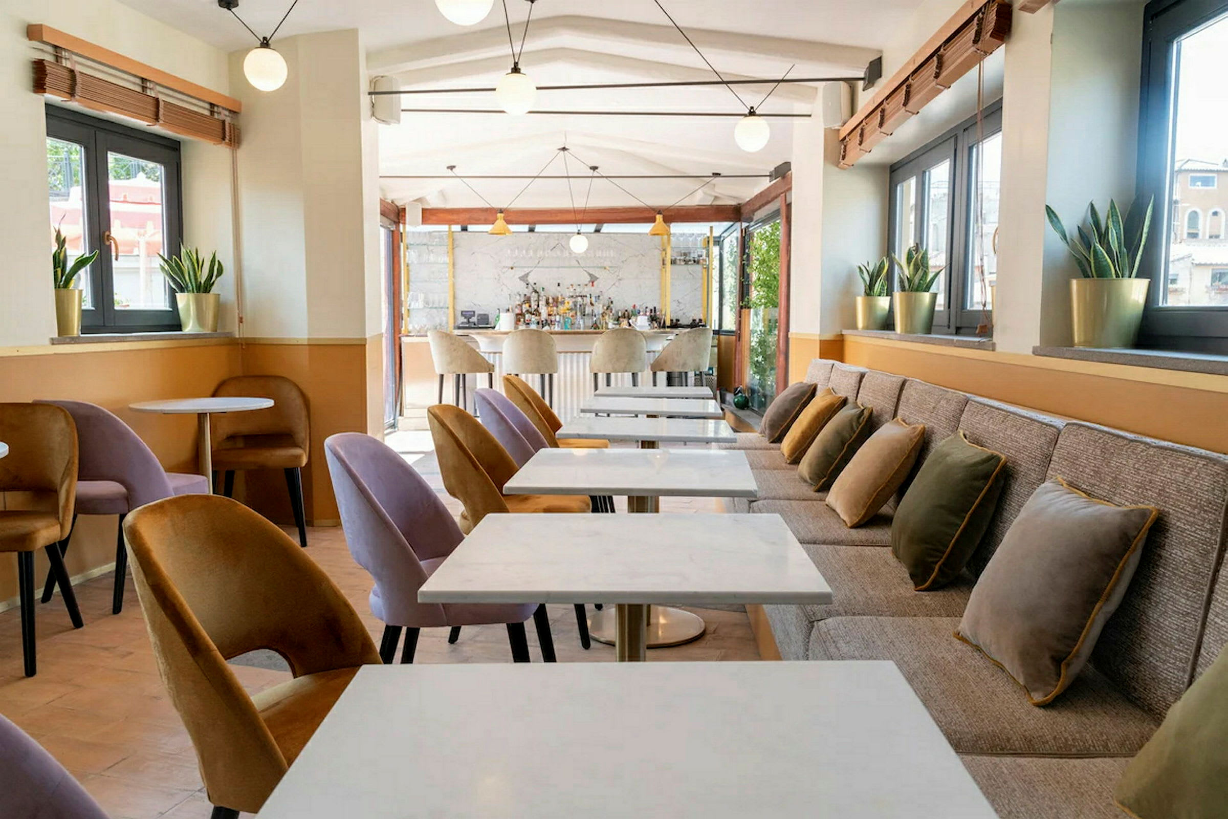 En moderne kafé med marmorbord, polstrede stoler og puter på en lang benk. (AI-generert tekst)