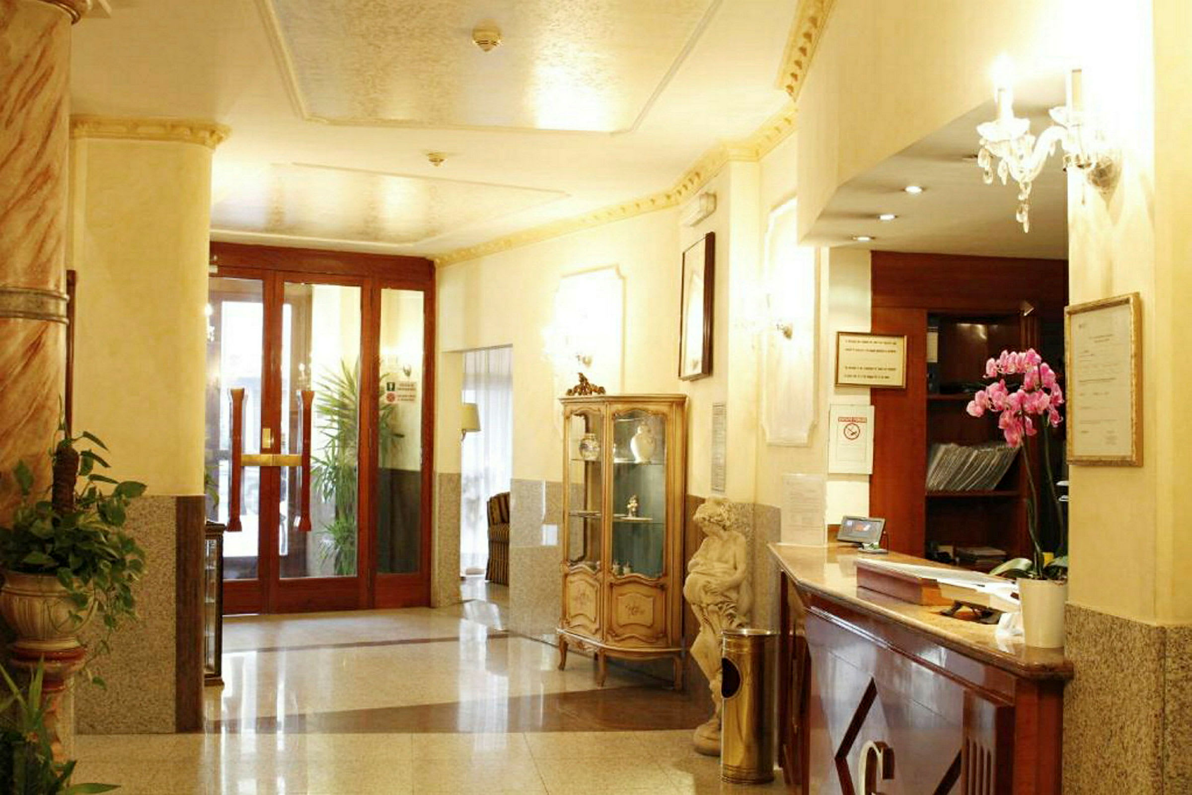Interiør av en hotellobby med resepsjon, glasskap, planter og ornamenter. (AI-generert tekst)