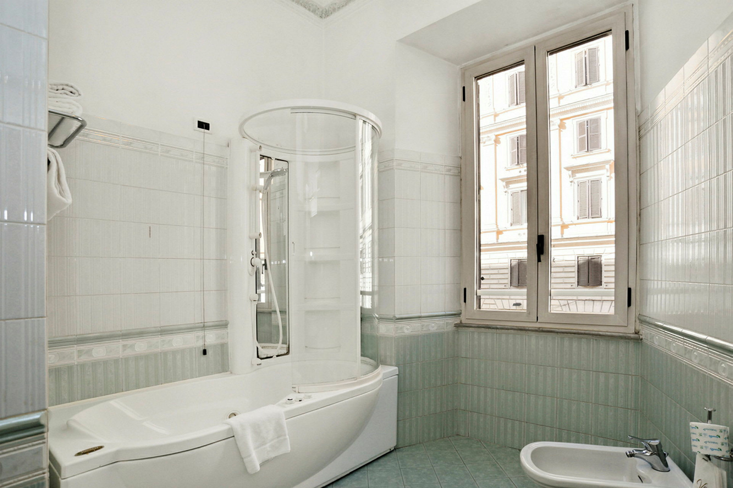Et lyst bad med stort vindu, hvitt badekar med dusj og liten bidet. (AI-generert tekst)