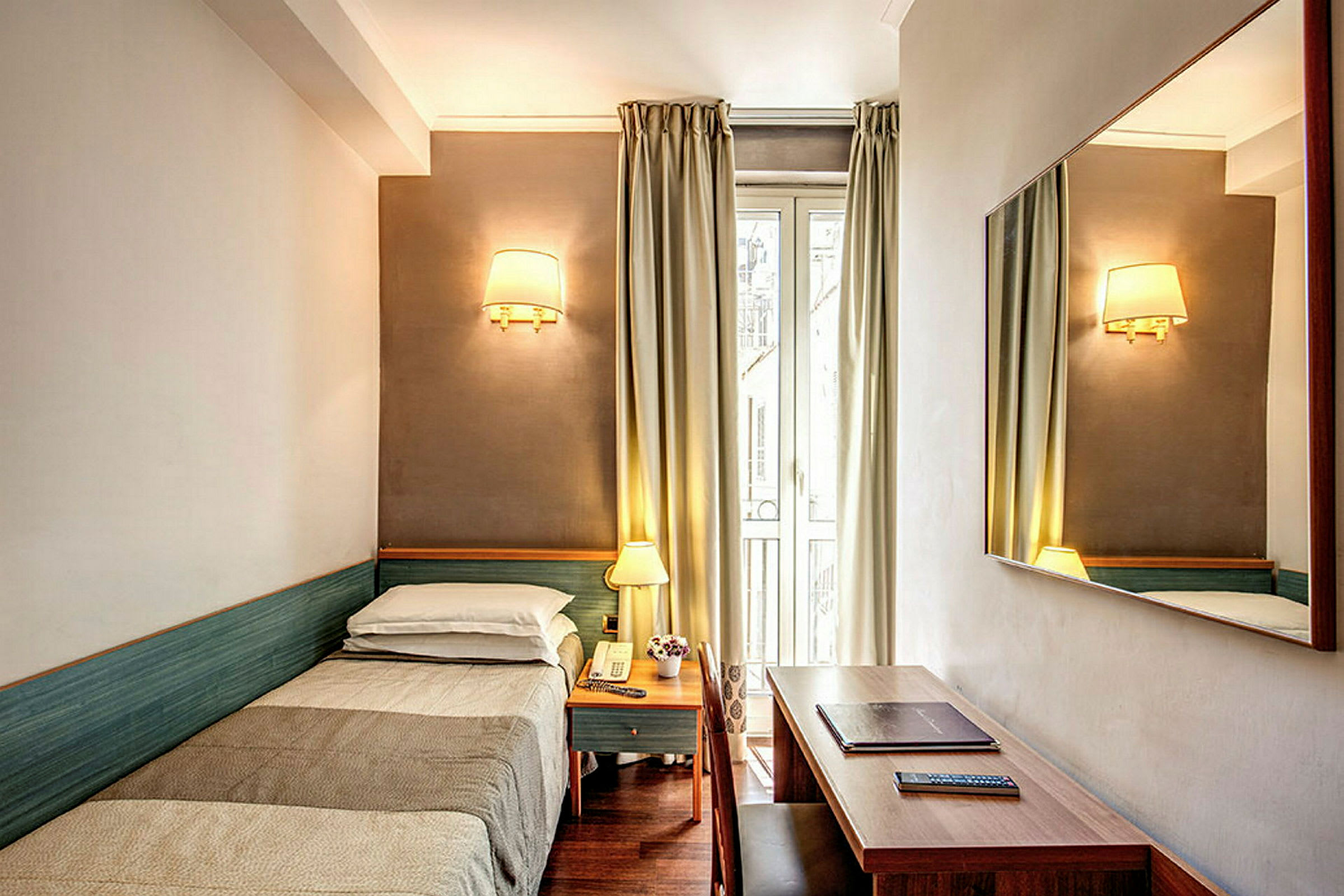 Et hotellrom med enkeltseng, nattbord, et speil på veggen og et skrivebord. (AI-generert tekst)