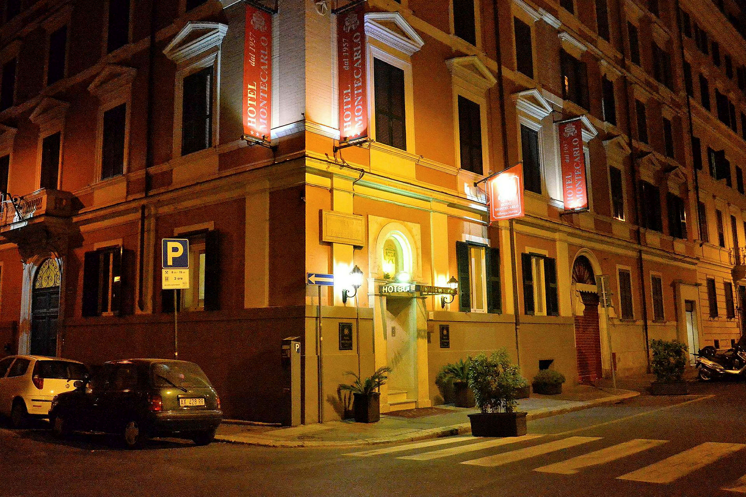 Et hotell med navnet Hotel Montecarlo ligger i et gatehjørne om kvelden. (AI-generert tekst)