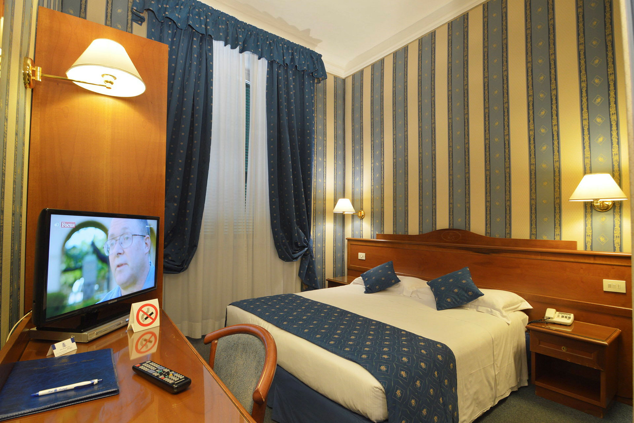 Et hotellrom med en dobbeltseng, nattbord og et skrivebord med en TV. (AI-generert tekst)