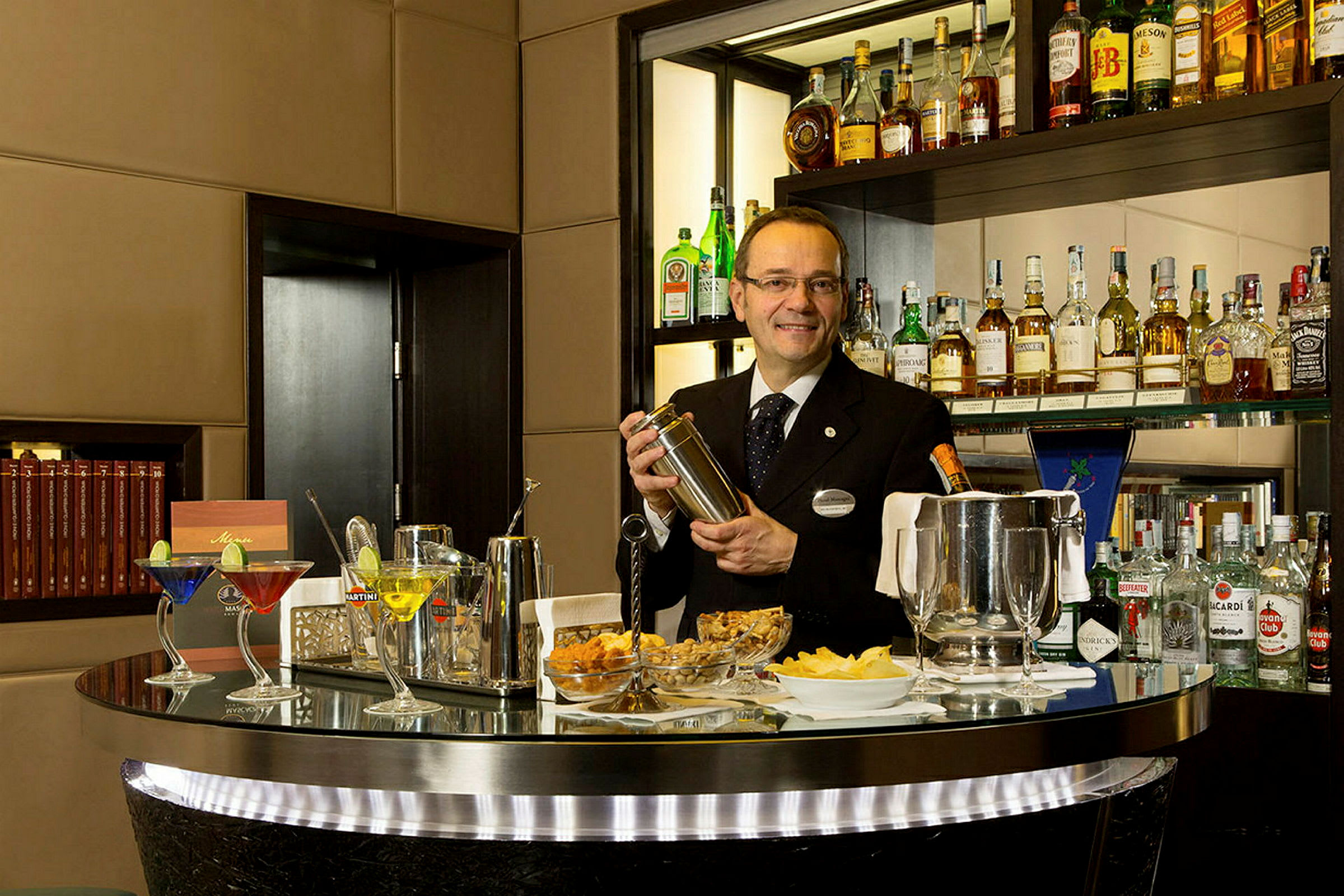 En bartender holder en shaker ved en bardisk fylt med flasker og cocktails. (AI-generert tekst)