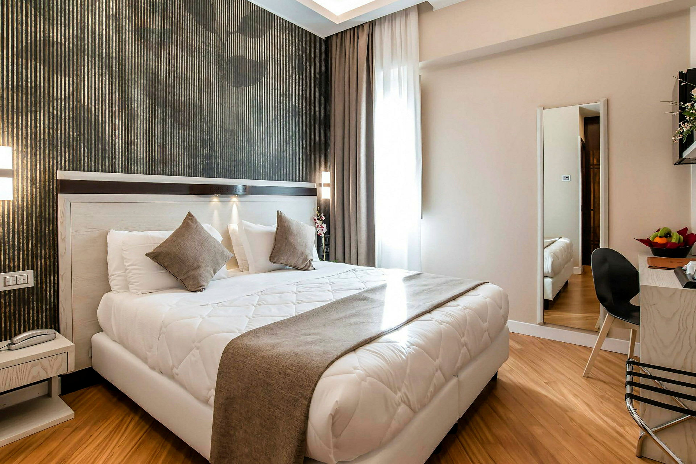 Moderne innredet hotellrom med dobbeltseng, nattbord, speil og sitteområde. (AI-generert tekst)