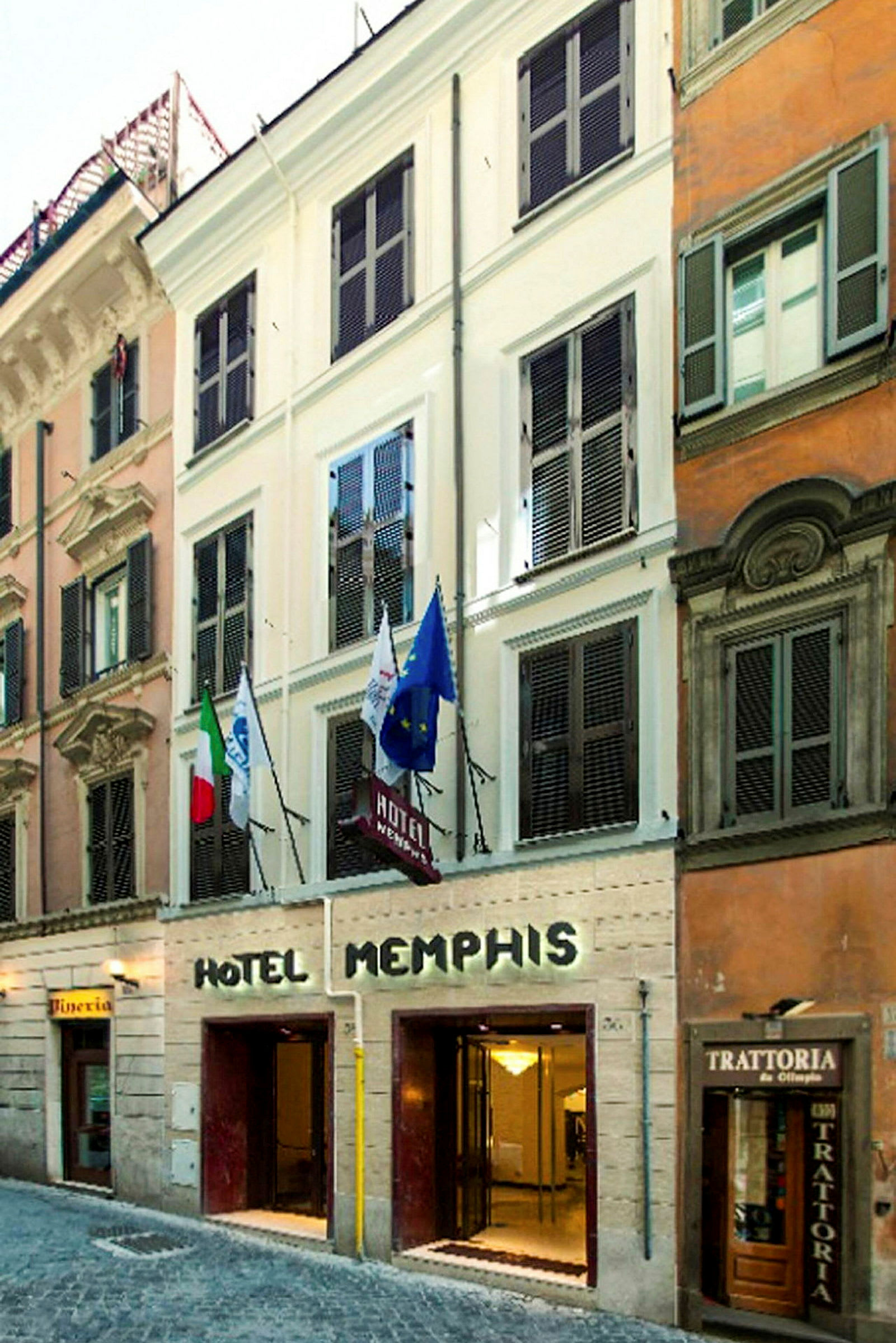 Fasaden til Hotel Memphis med inngang i gateplan og flagg synlige over. (AI-generert tekst)