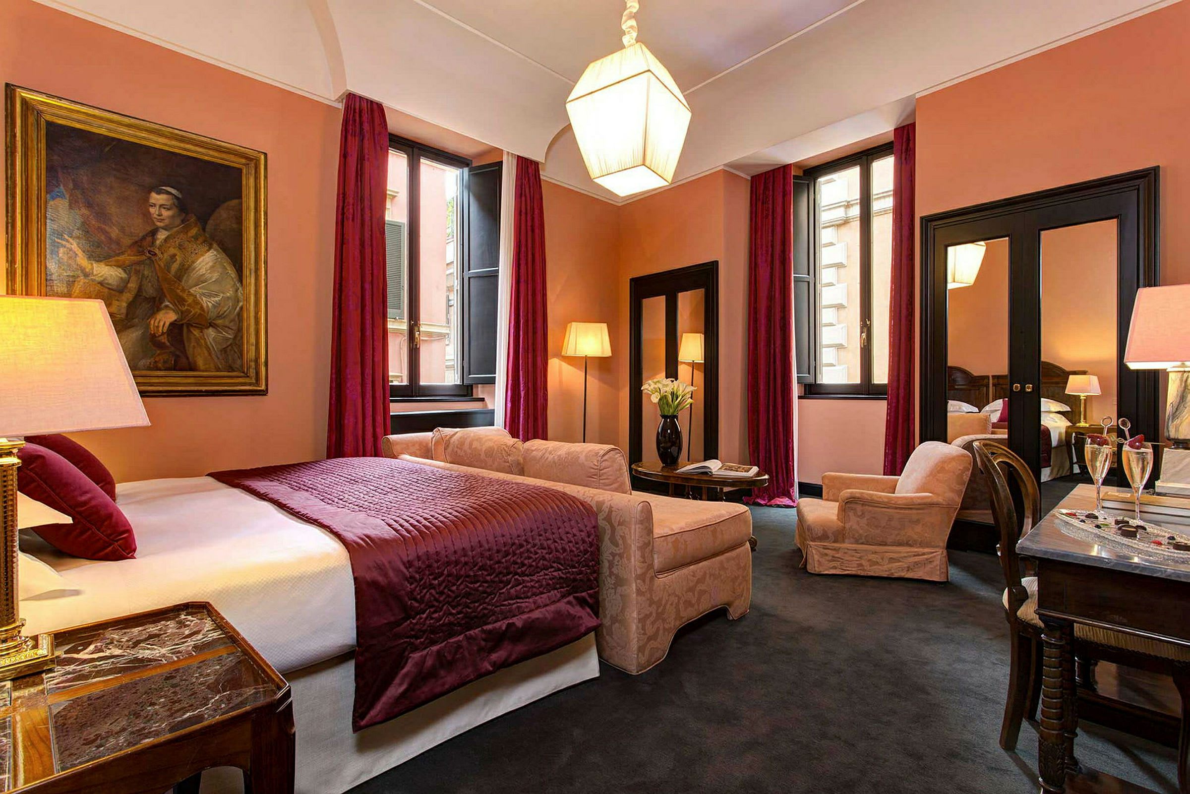 Et elegant hotellrom med en dobbeltseng, lilla sengeteppe og matchende gardiner, sammen med komfortable lenestoler og et bord. (AI-generert tekst)