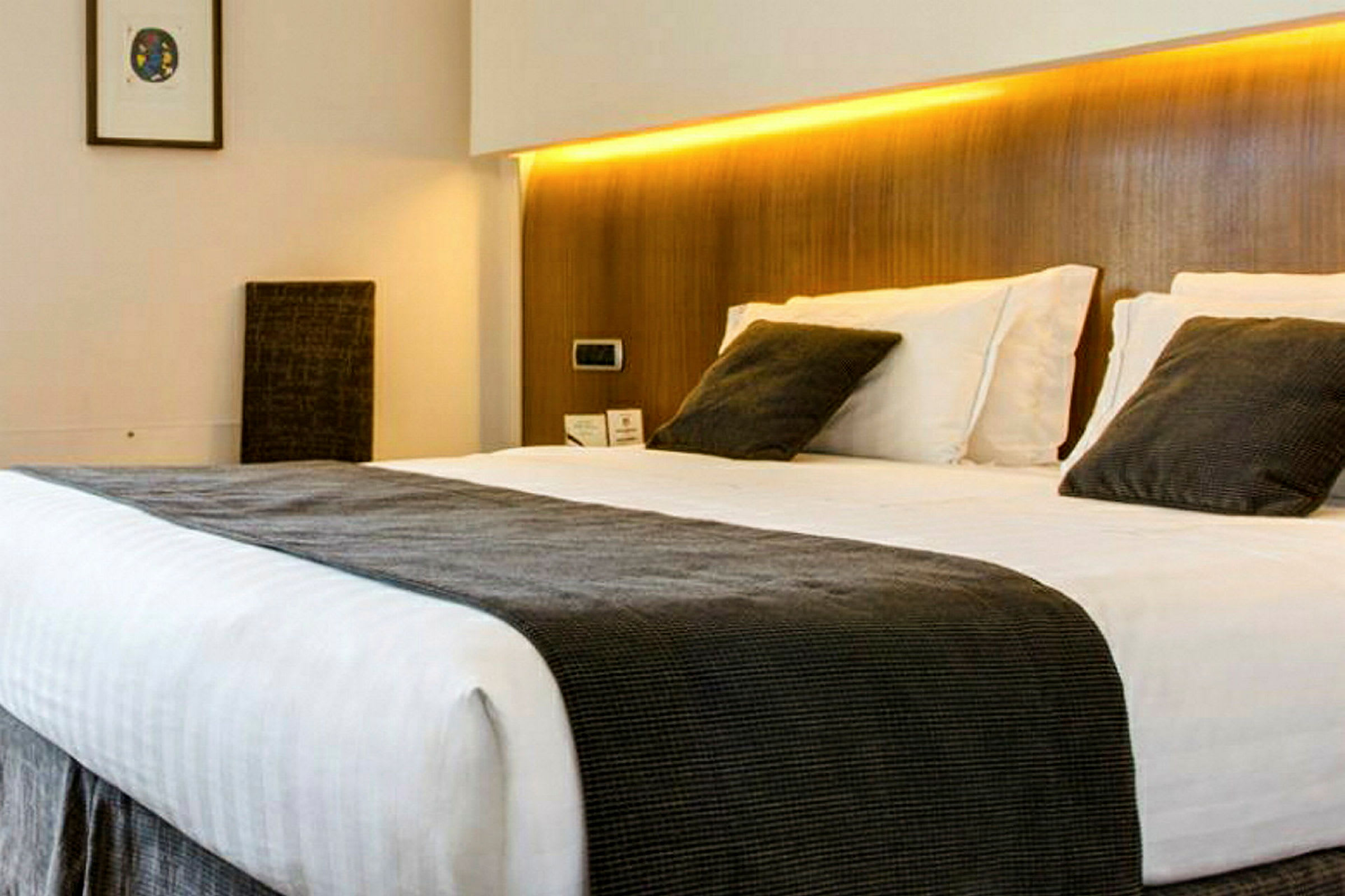 Bilde av en oppredd seng med hvite laken og grå puter i et hotellrom. (AI-generert tekst)