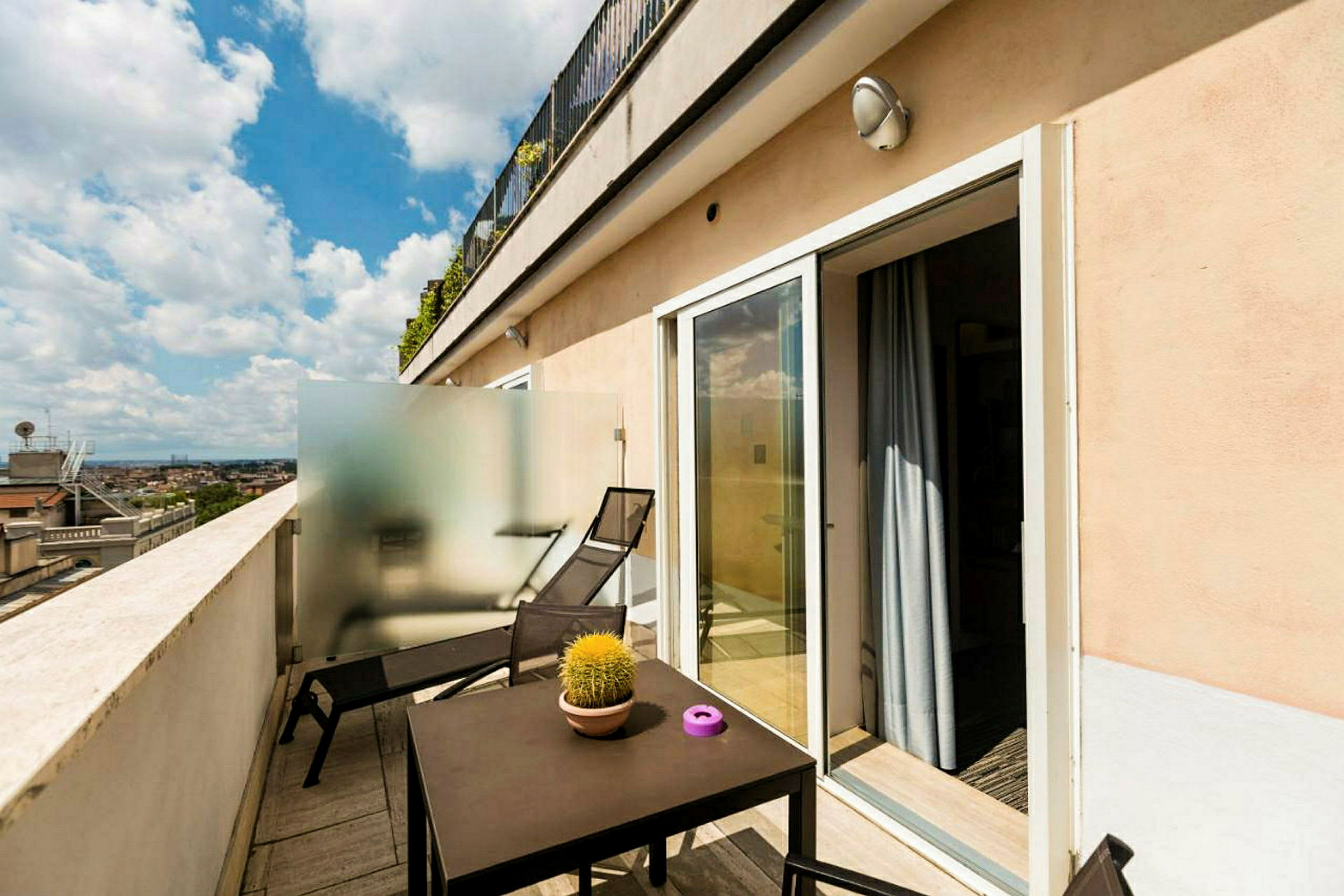 En terrasse med bord, stoler og solsenger, samt utsikt over byens tak. (AI-generert tekst)