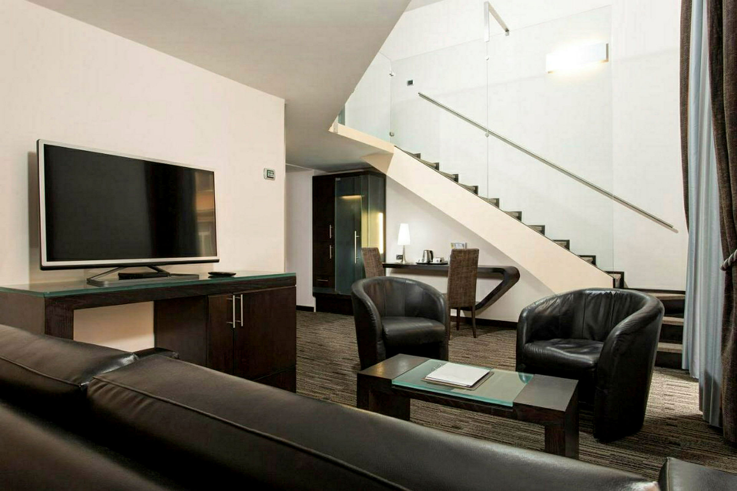 Et moderne innredet hotellrom med en sofa, lenestoler, TV og en trapp til et loft. (AI-generert tekst)