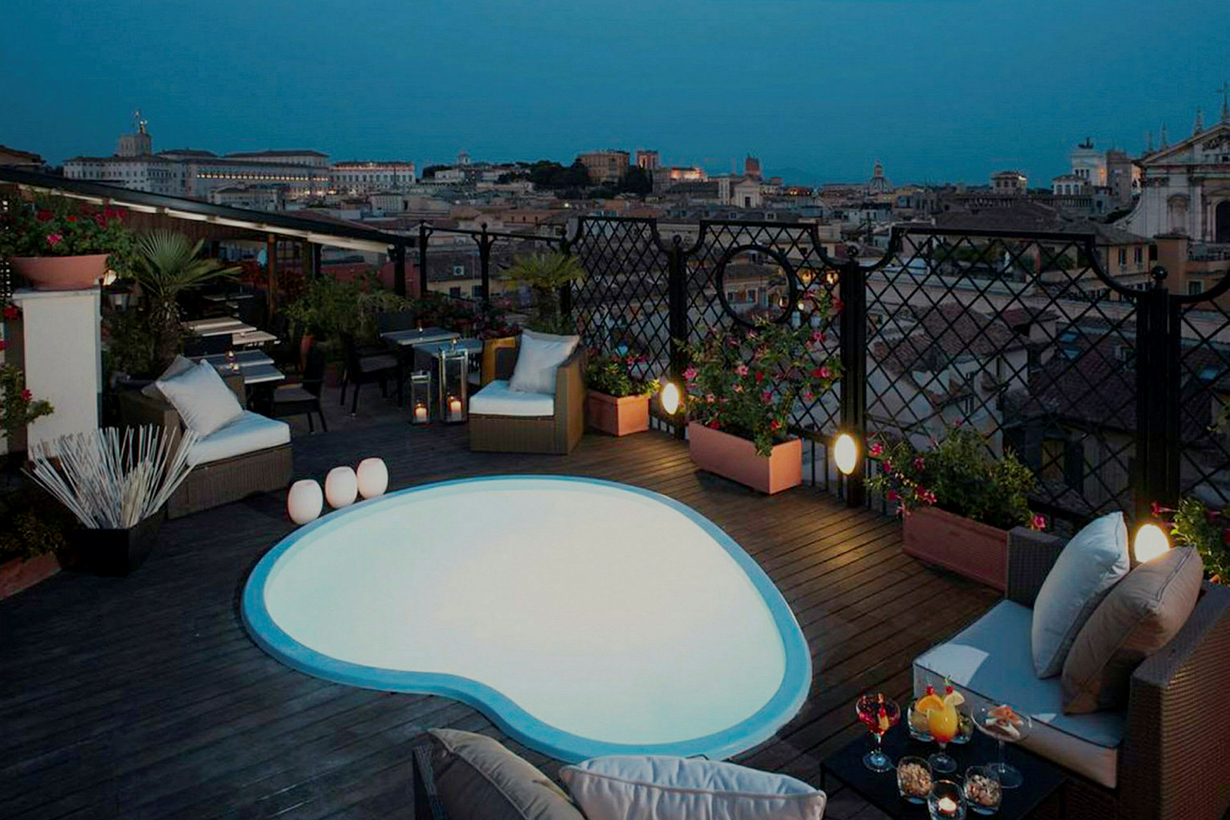 Bilde av en takterrasse med et lite basseng og sittemøbler, samt utsikt over en by i skumringen. (AI-generert tekst)