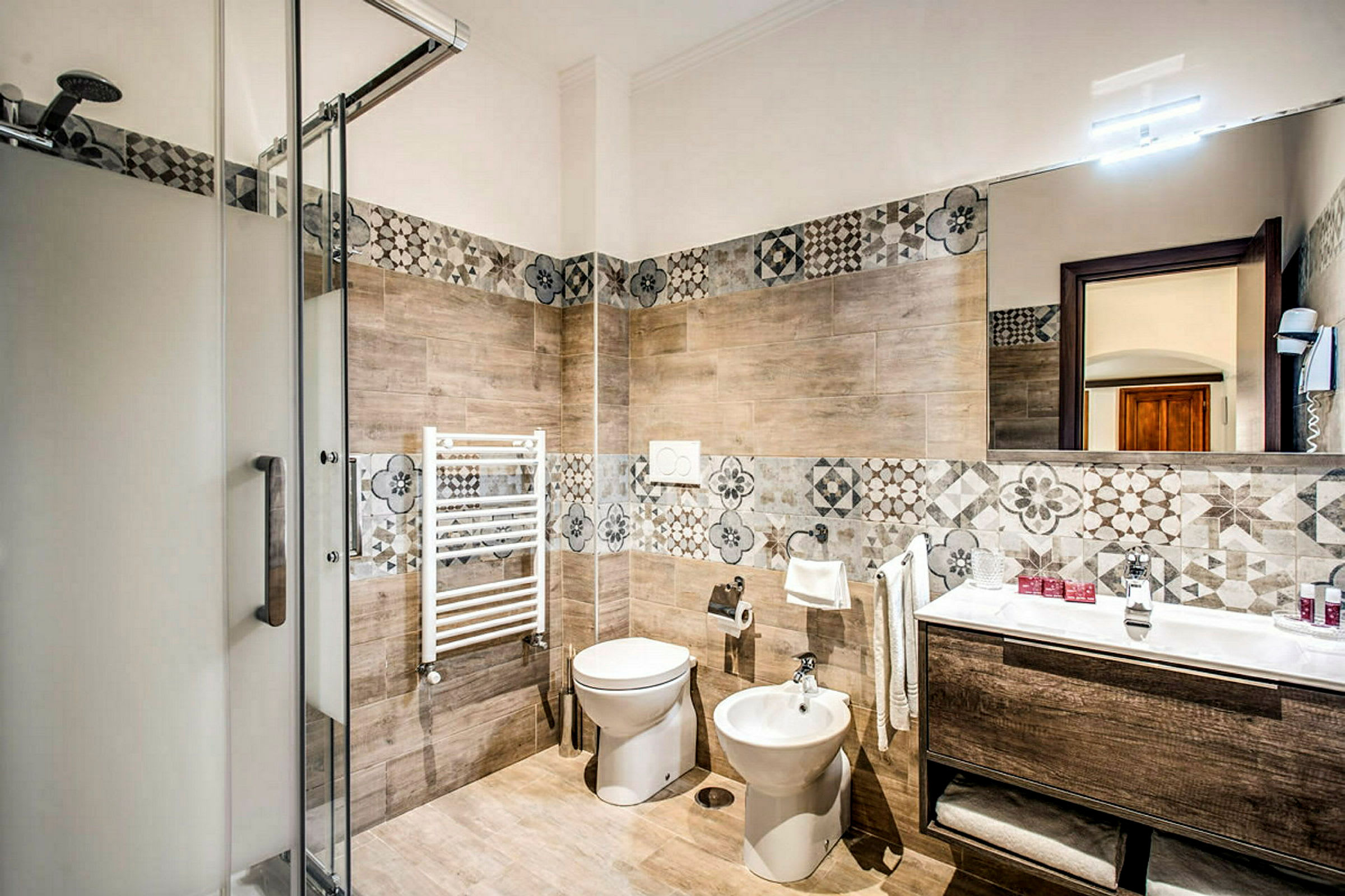 Et bad med dusjkabinett, toalett, bidet, servant og dekorative veggfliser. (AI-generert tekst)