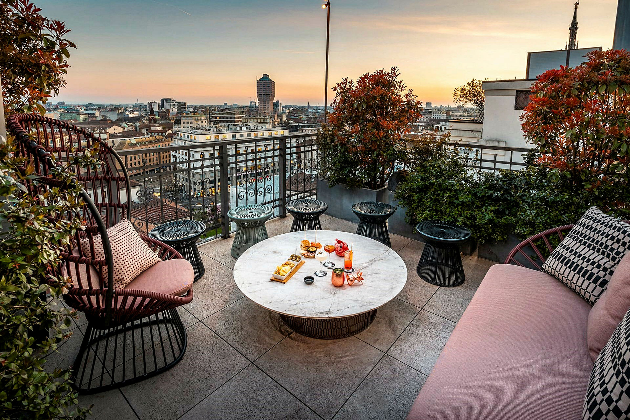 Terrasse med utsikt over byen ved solnedgang, møbler og bord med mat og drikke. (AI-generert tekst)