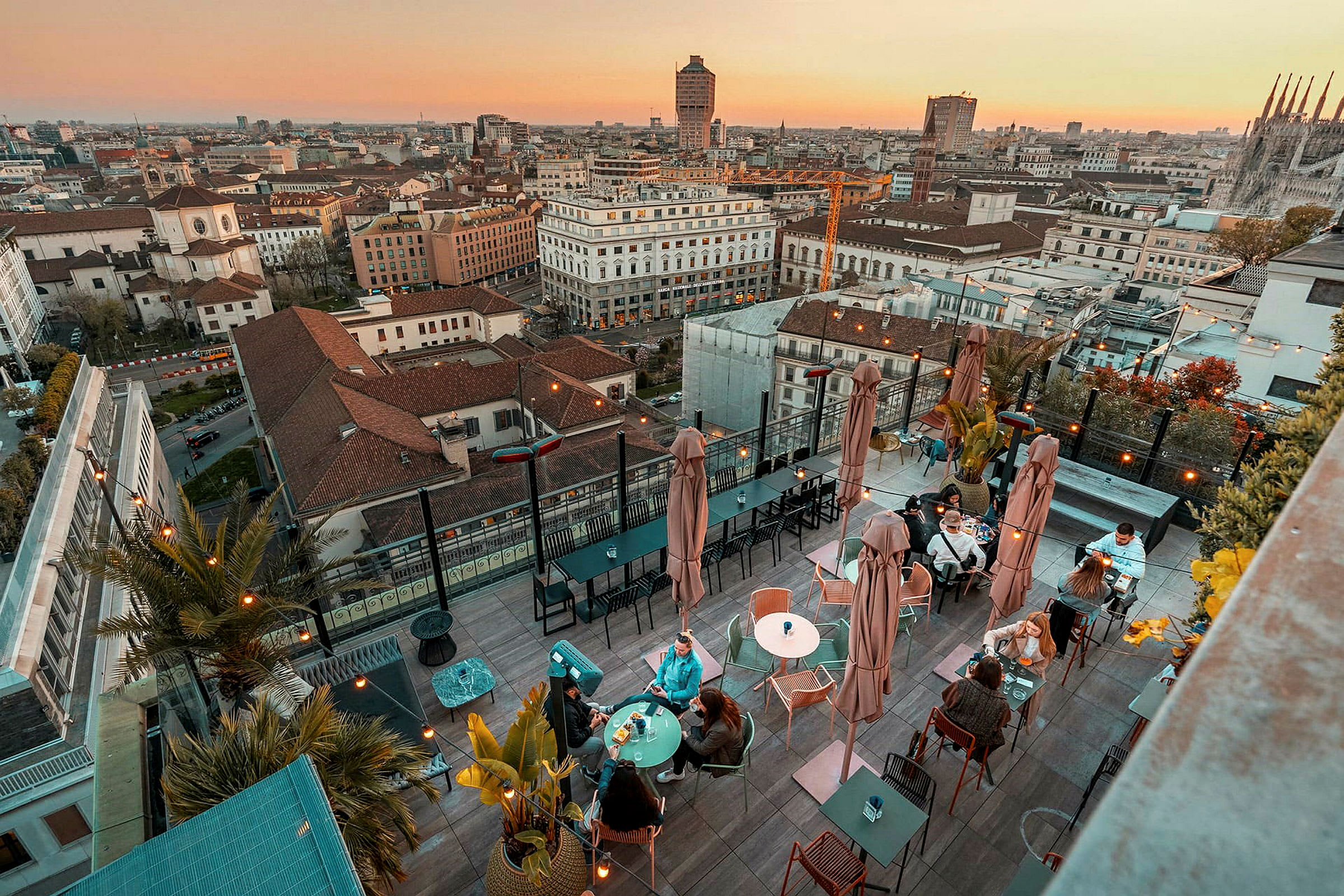 En takterrasse med bord og sitteplasser, omgitt av panoramautsikt over en by ved solnedgang. (AI-generert tekst)