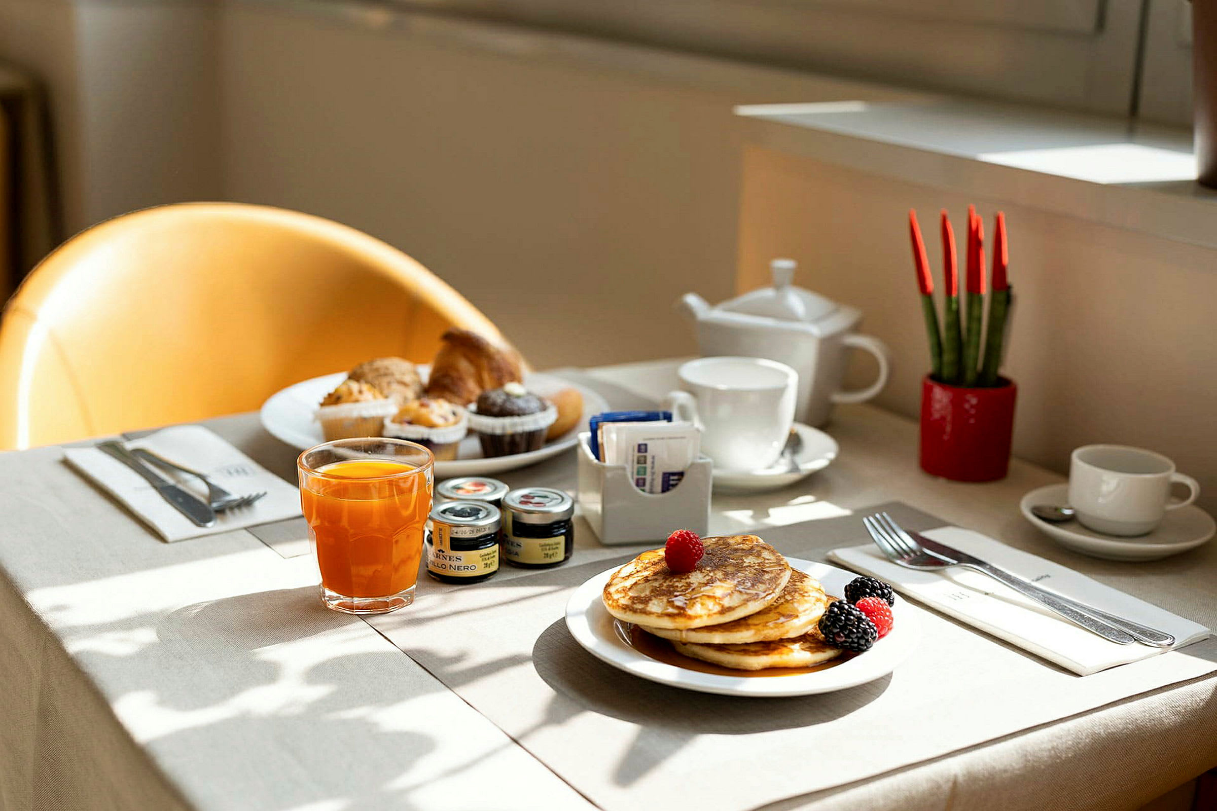 En oppdekket frokost med pannekaker, frukt, juice og muffins på et bord. (AI-generert tekst)