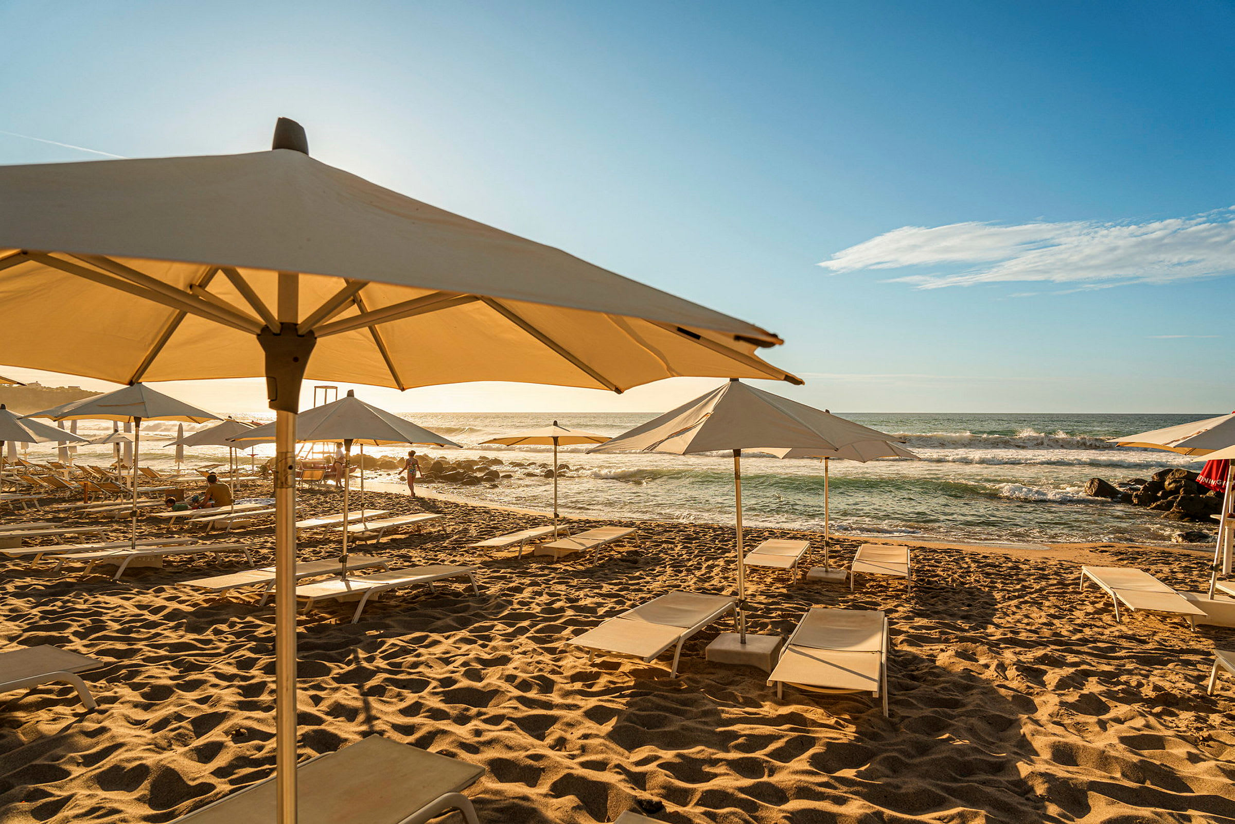 Solstoler med parasoller står plassert på en sandstrand ved havet. (AI-generert tekst)
