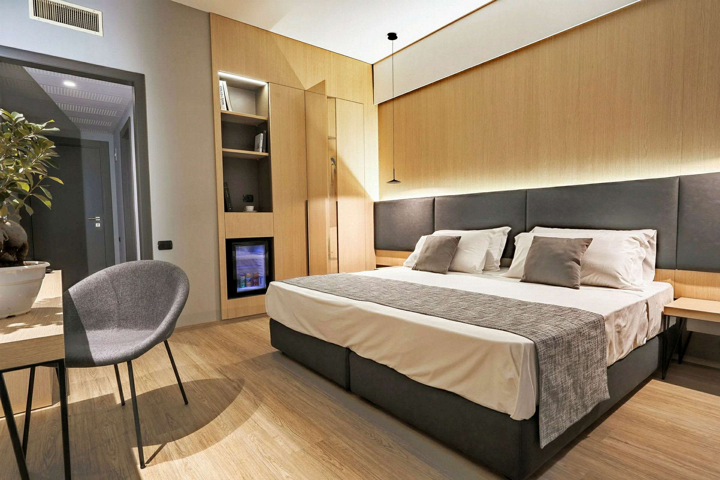Hotellrom med dobbeltseng, nattbord og en stol ved et bord. (AI-generert tekst)