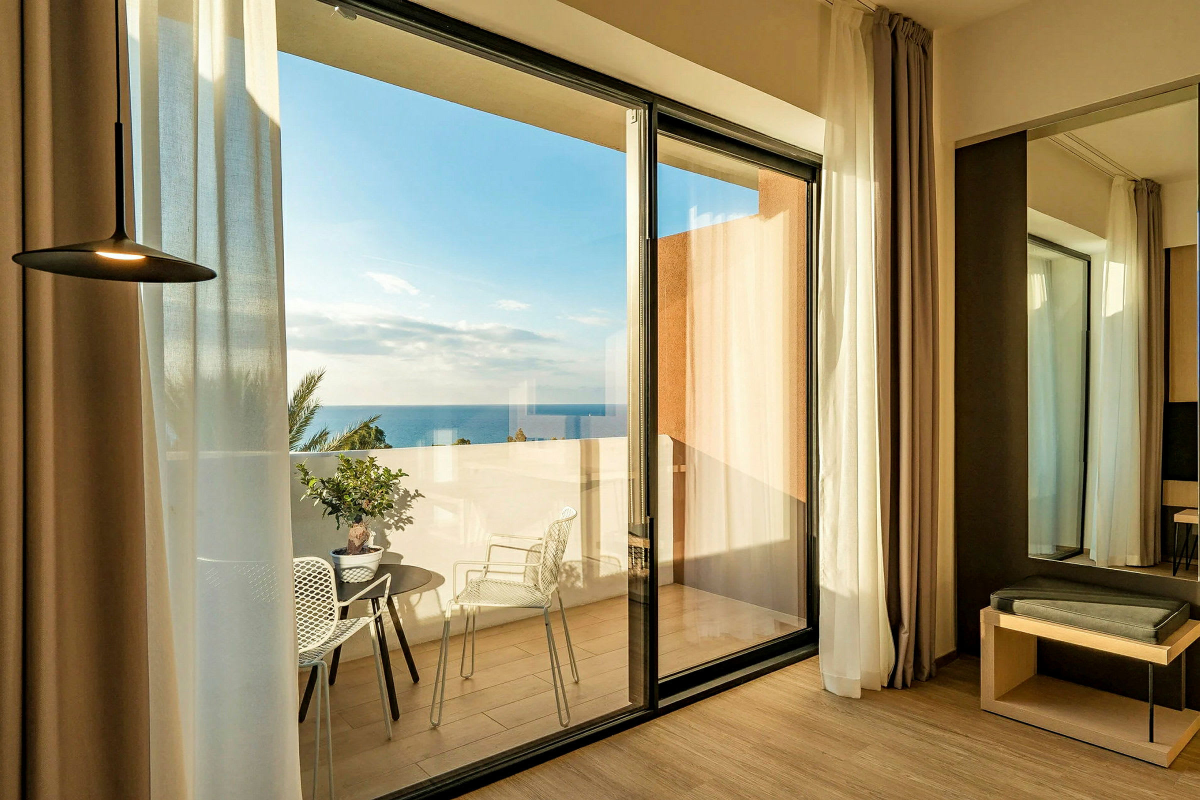 Hotellrom med glassdører som fører ut til en terrasse med havutsikt. (AI-generert tekst)