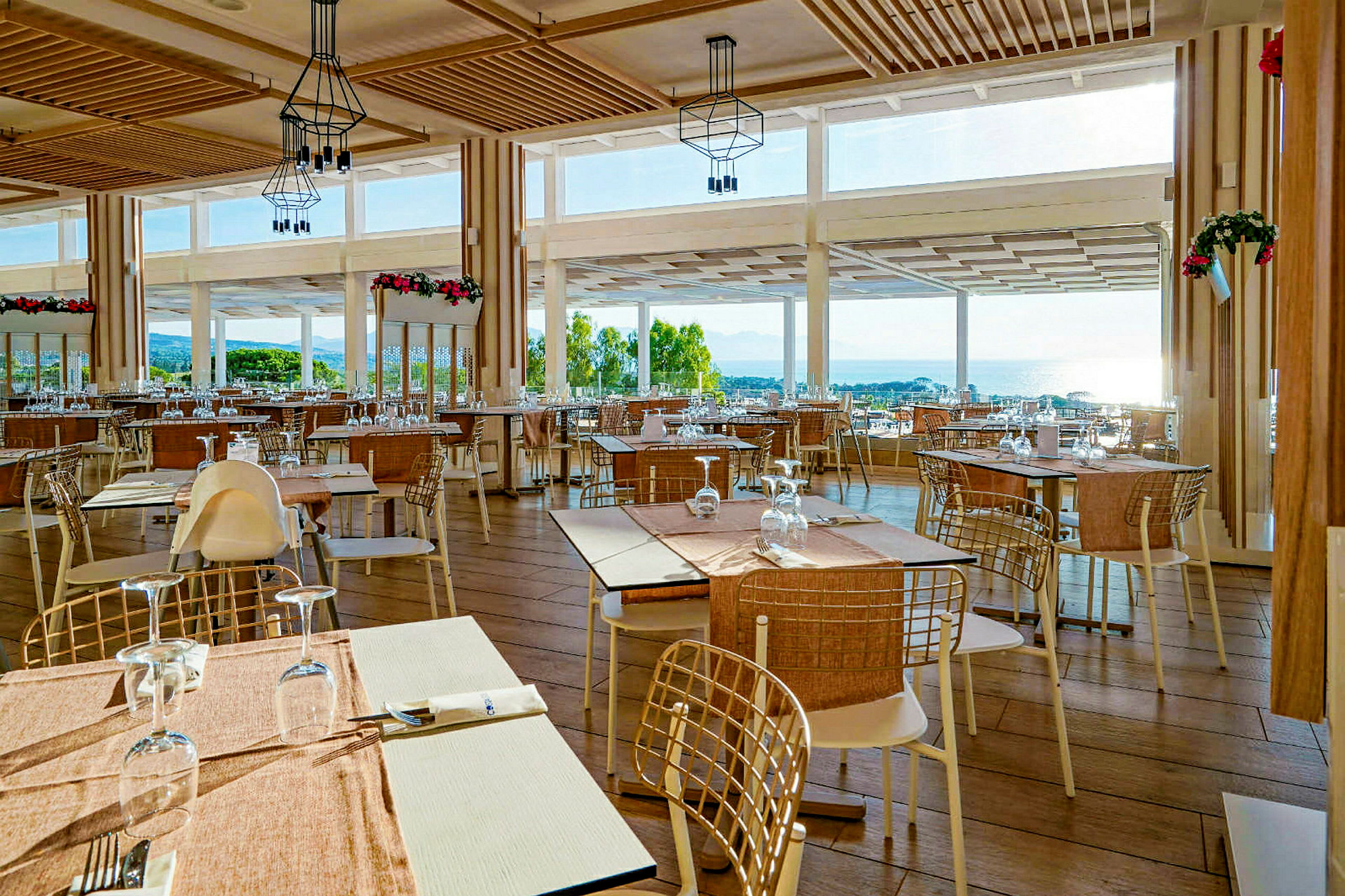 En restaurant med bord og stoler, store vinduer med utsikt over landskapet og havet. (AI-generert tekst)