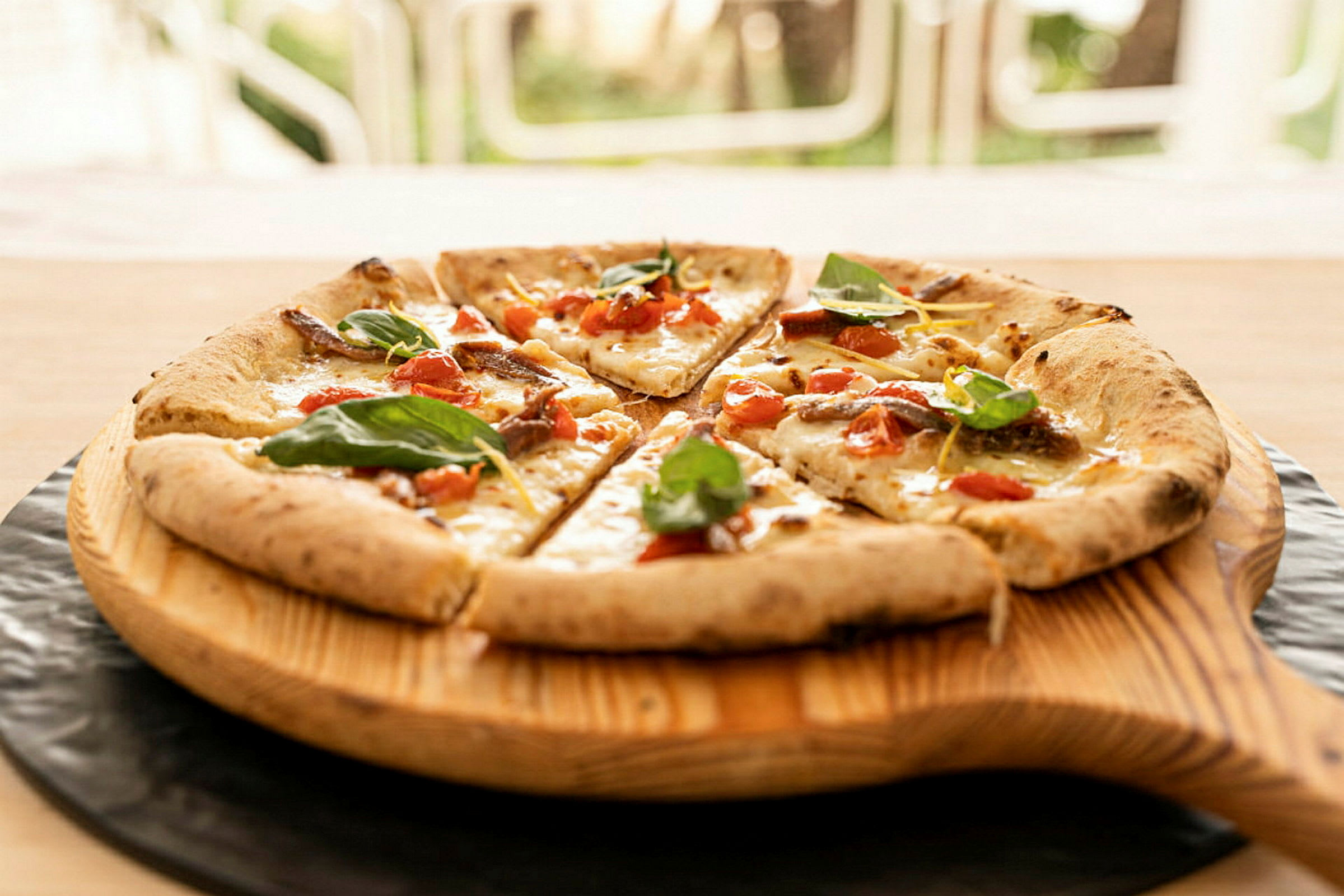 En pizza med tomat, ost og bladkrydder servert på en treplate. (AI-generert tekst)