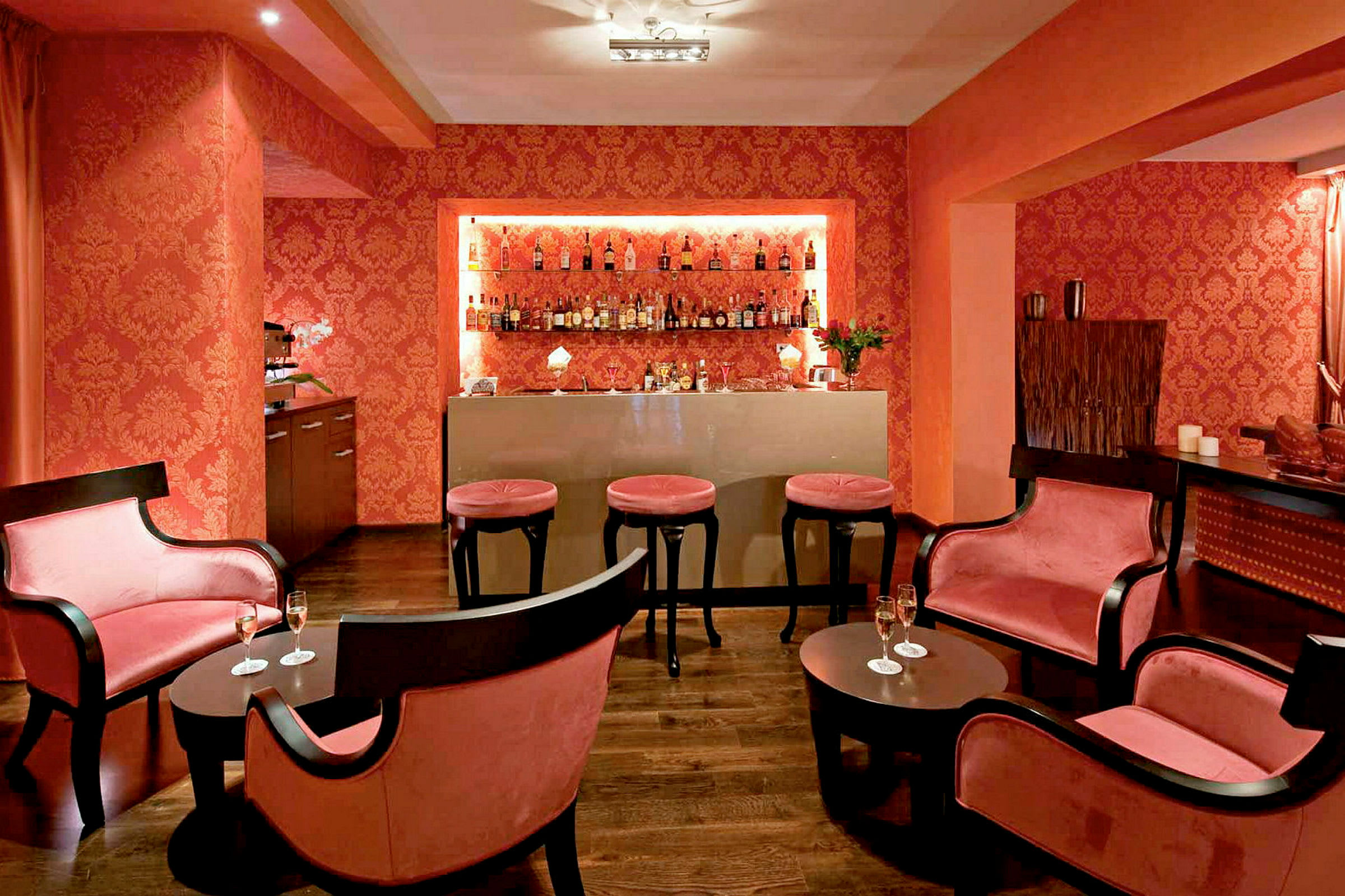 Bilde som viser et elegant område innredet som en cocktailbar med mørke møbler, rosa puter og flasker på en hylle. (AI-generert tekst)
