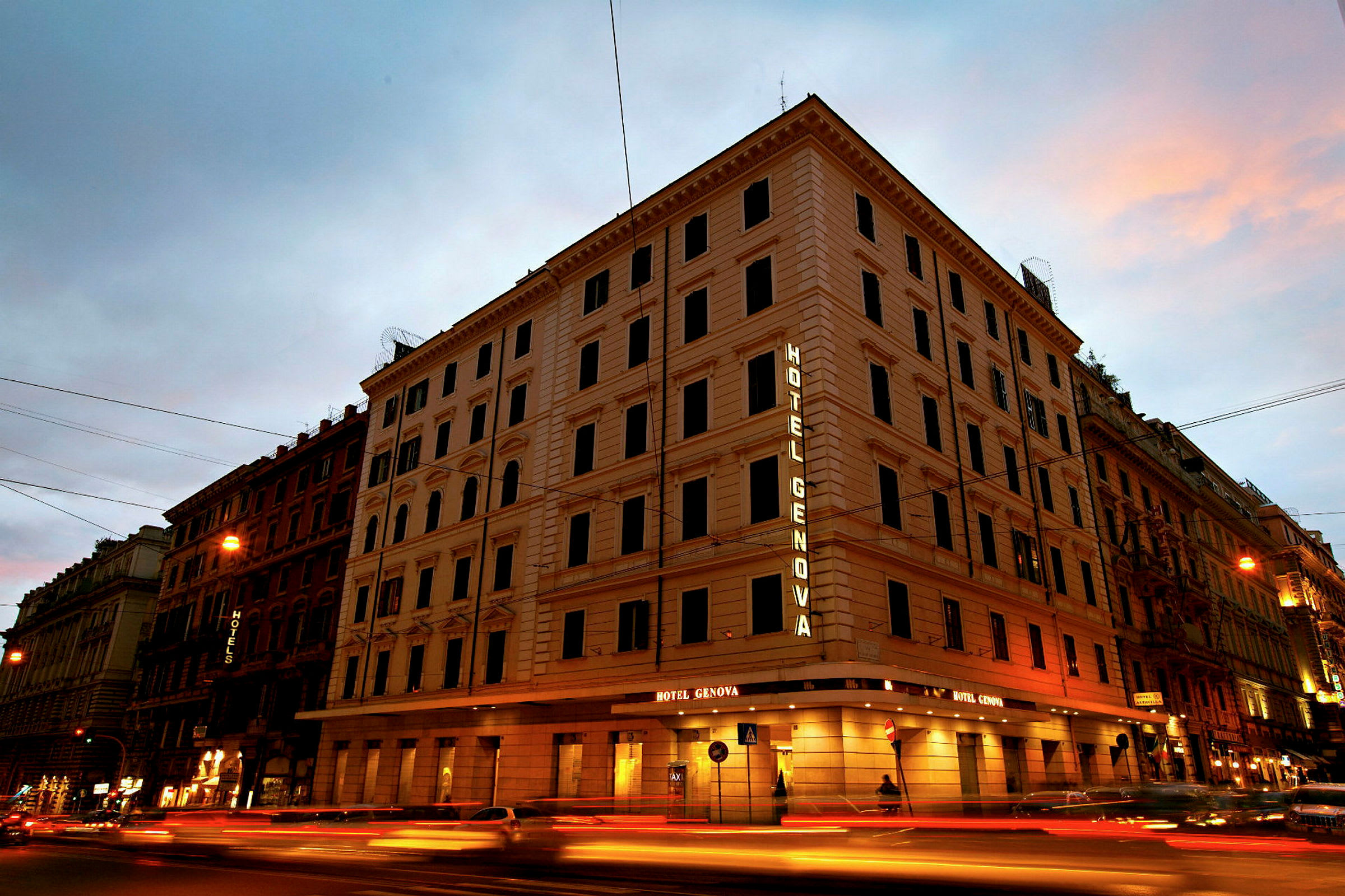En fleretasjes bygning med teksten Hotel Genova som lyser på fasaden. (AI-generert tekst)