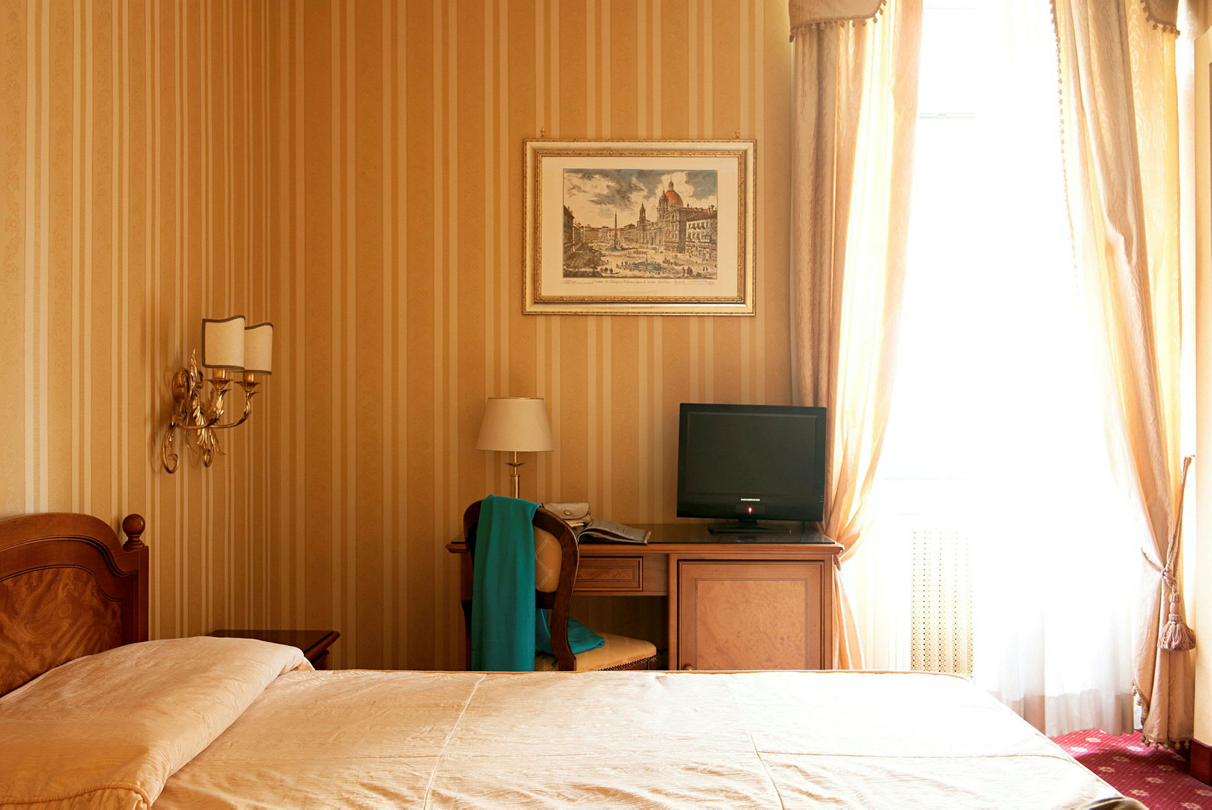 Et hotellrom med en seng, nattbord, skrivebord med en stol og en TV, samt gule vegger og gardiner. (AI-generert tekst)