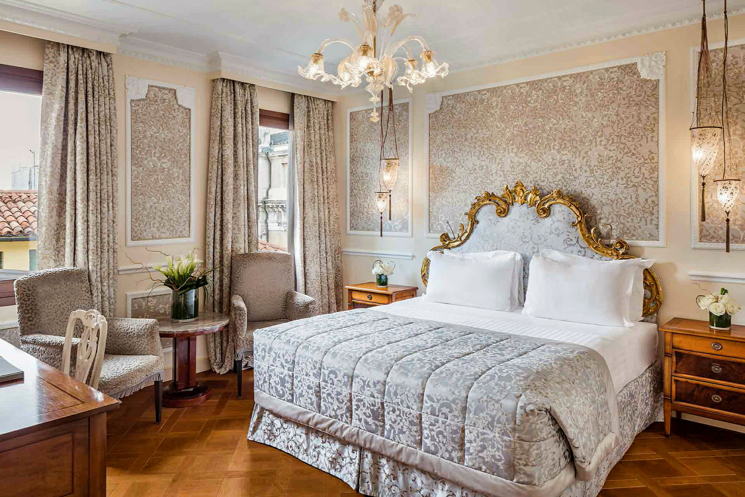 Et elegant soverom med en stor seng med dekorert sengegavl, to lenestoler og et bord med en vase med blomster. (AI-generert tekst)