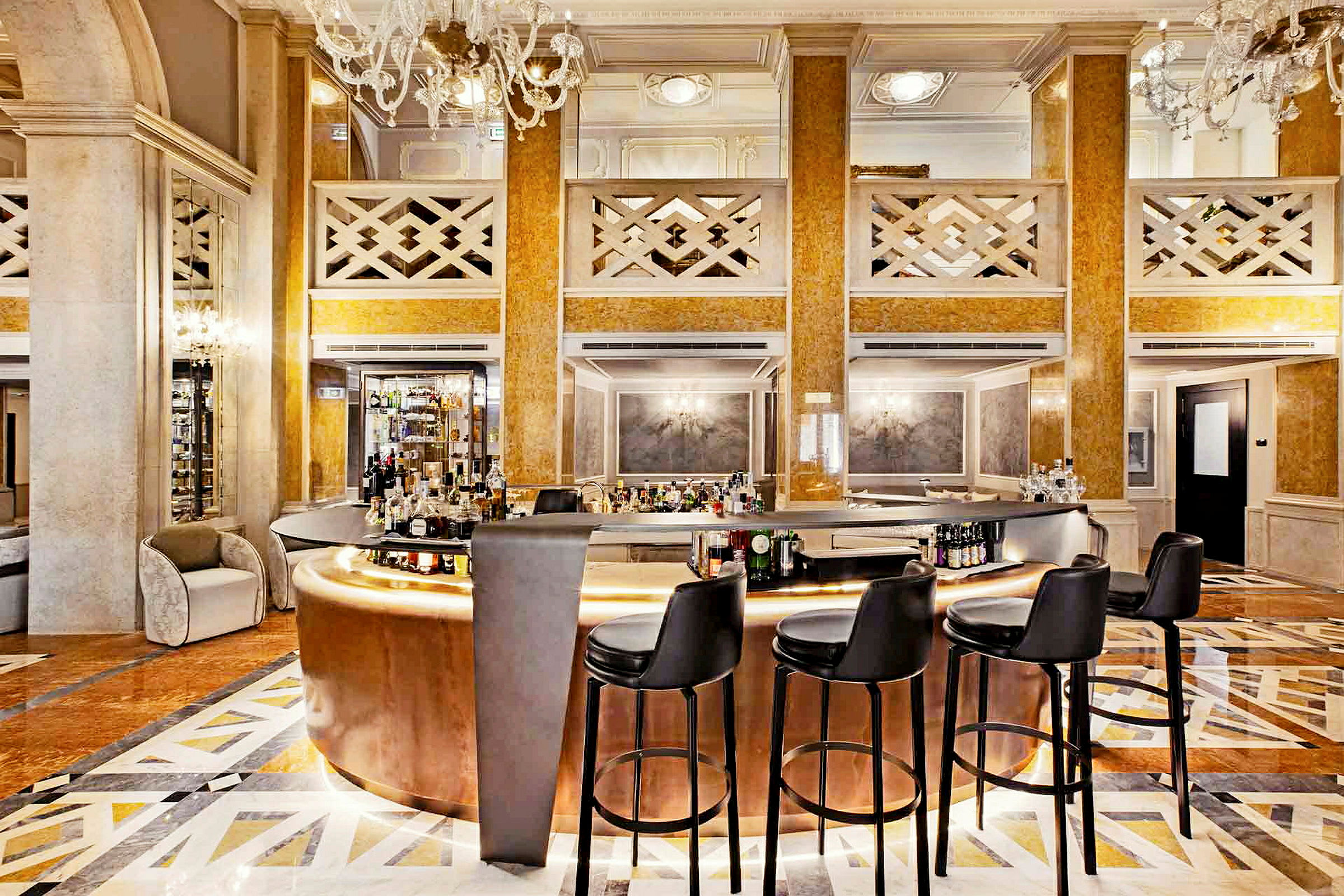 En elegant hotellbar, med polerte gul-tonede material og en velstelt gulvflate, omgitt av svarte barstoler og staselige lysekroner. (AI-generert tekst)