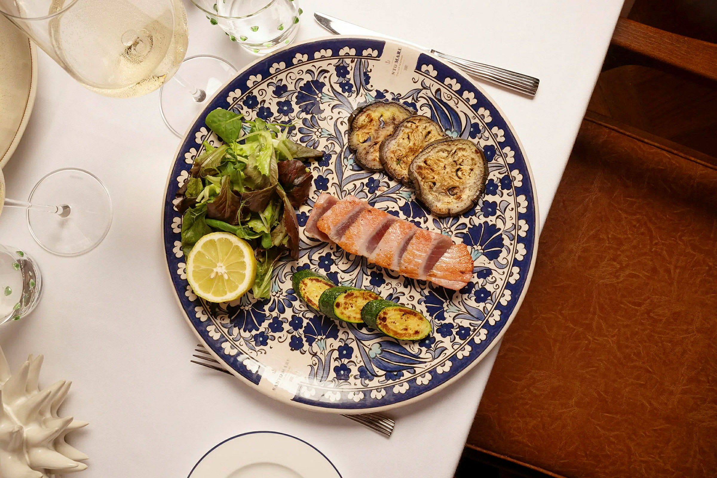 En tallerken med biter av laks, stekte grønnsaker og salat med en halv sitron på et dekket bord. (AI-generert tekst)