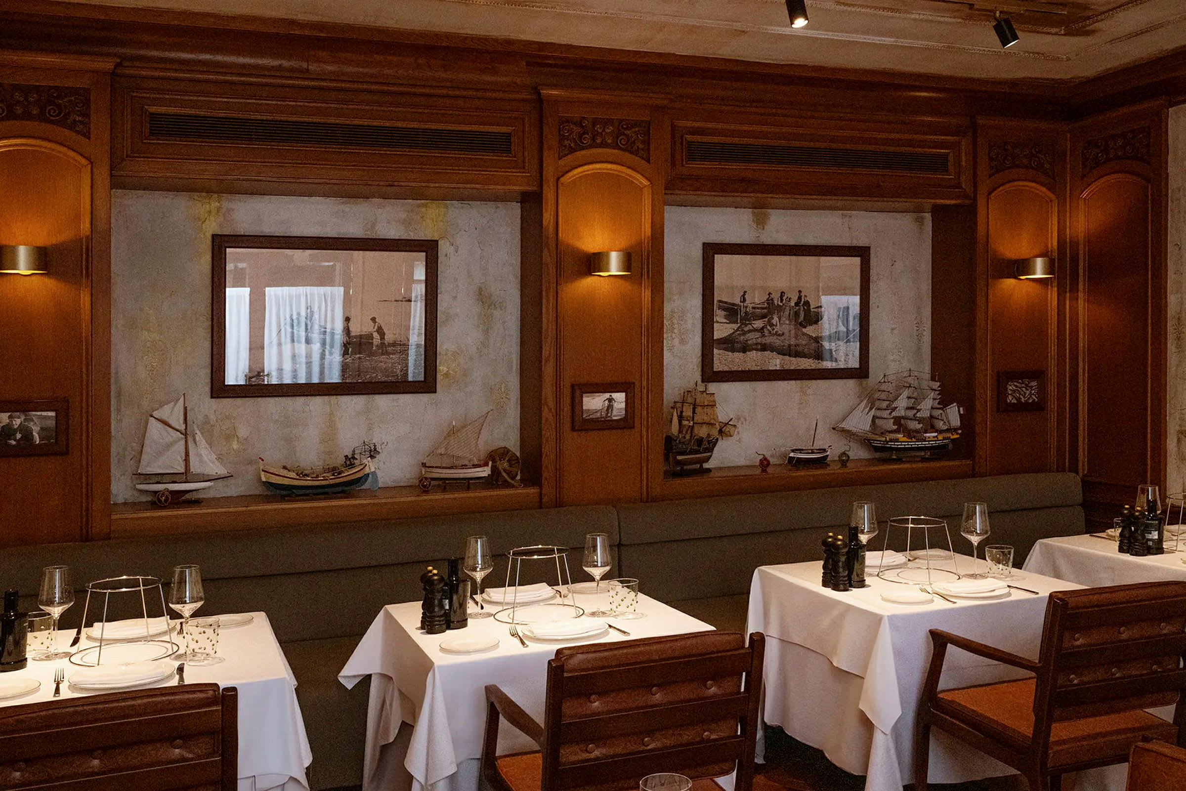 Et elegant restaurantinteriør med bord dekket med hvite duker og tremøbler. Veggene er dekorert med bilder og modellbåter. (AI-generert tekst)