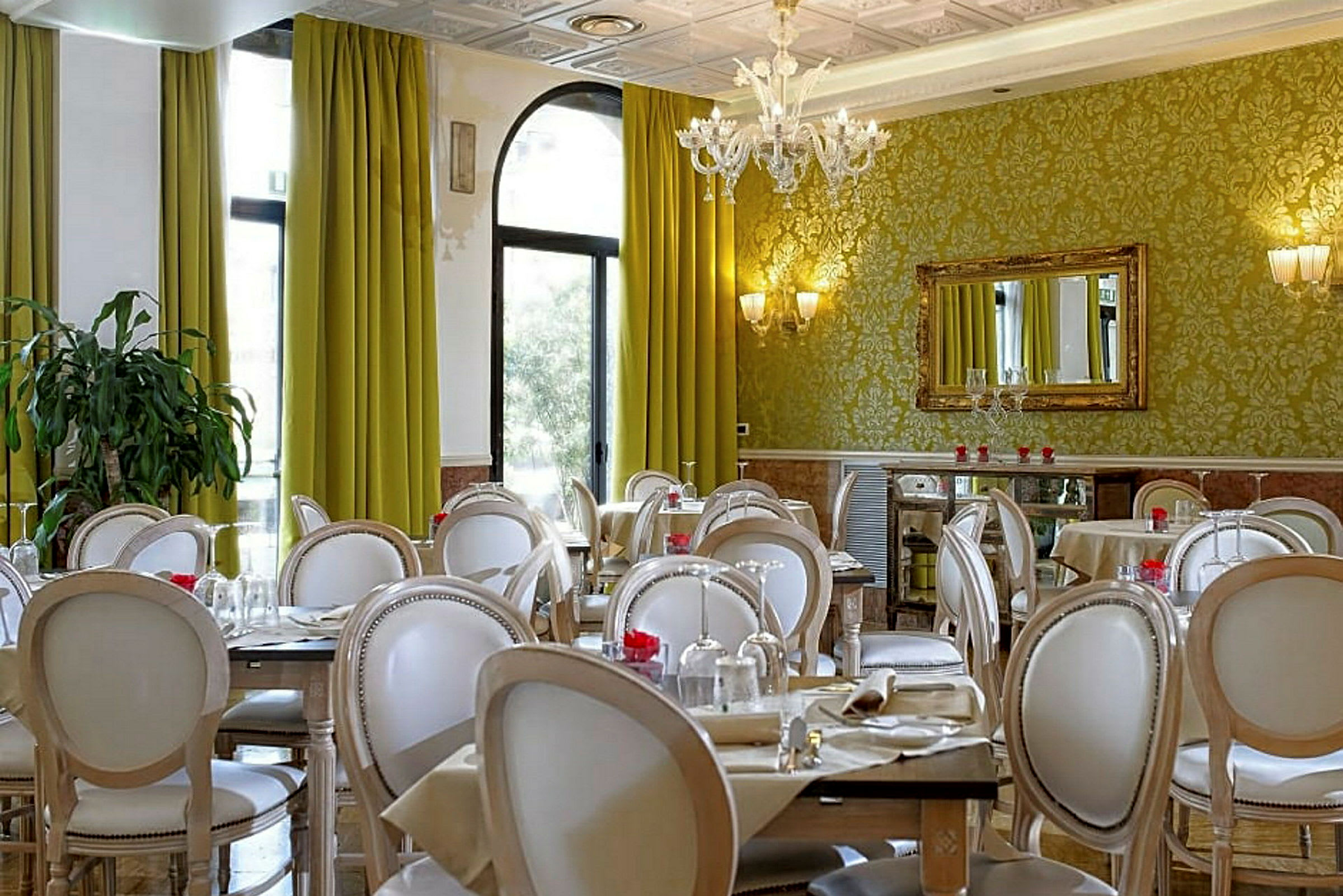 Et elegant innredet restaurantområde med grønne gardiner, dekorerte vegger og hvite stoler rundt dekte bord. (AI-generert tekst)