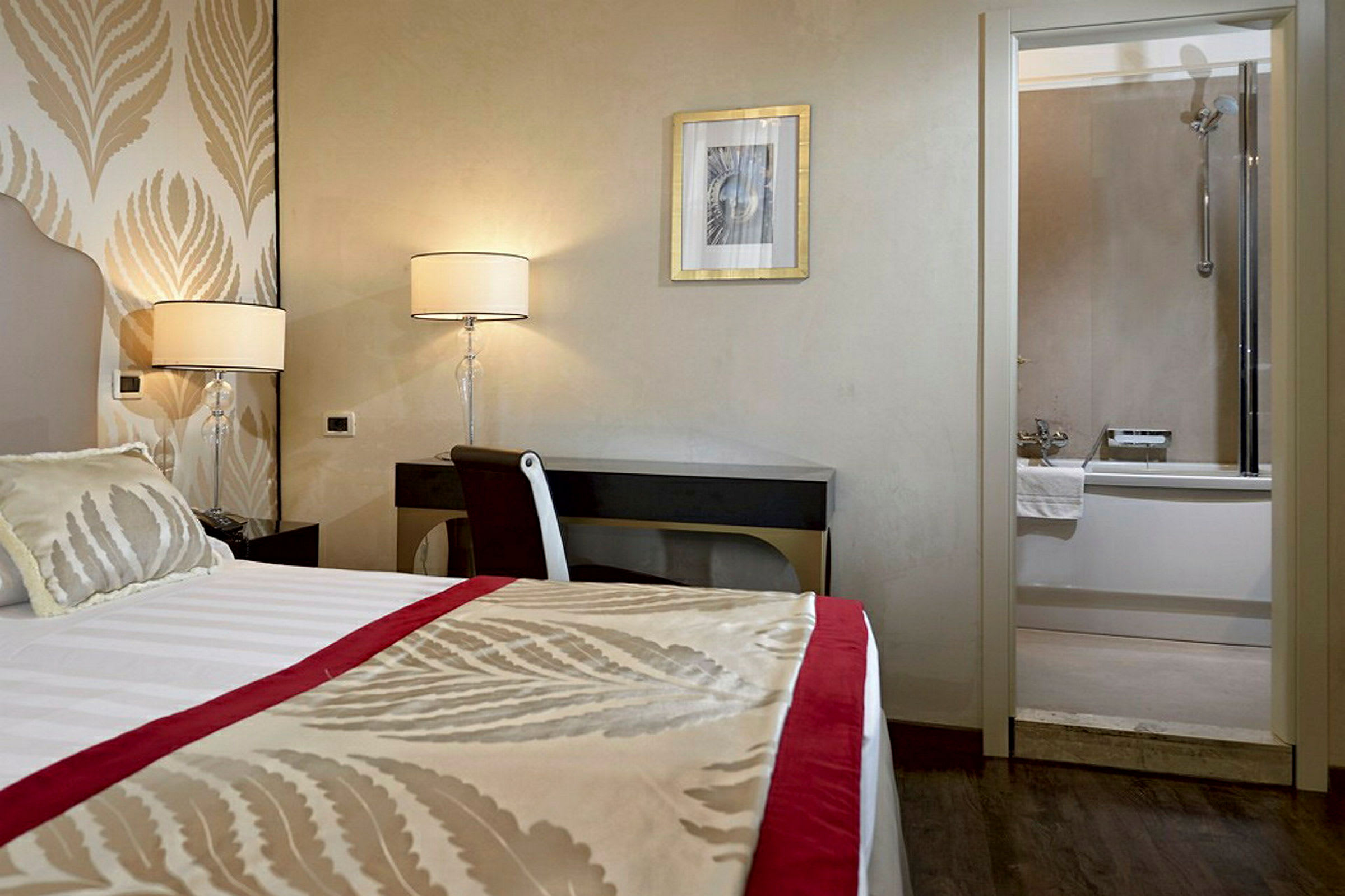 Hotellrom med en seng, skrivebord og lamper, samt et bad med badekar i bakgrunnen. (AI-generert tekst)