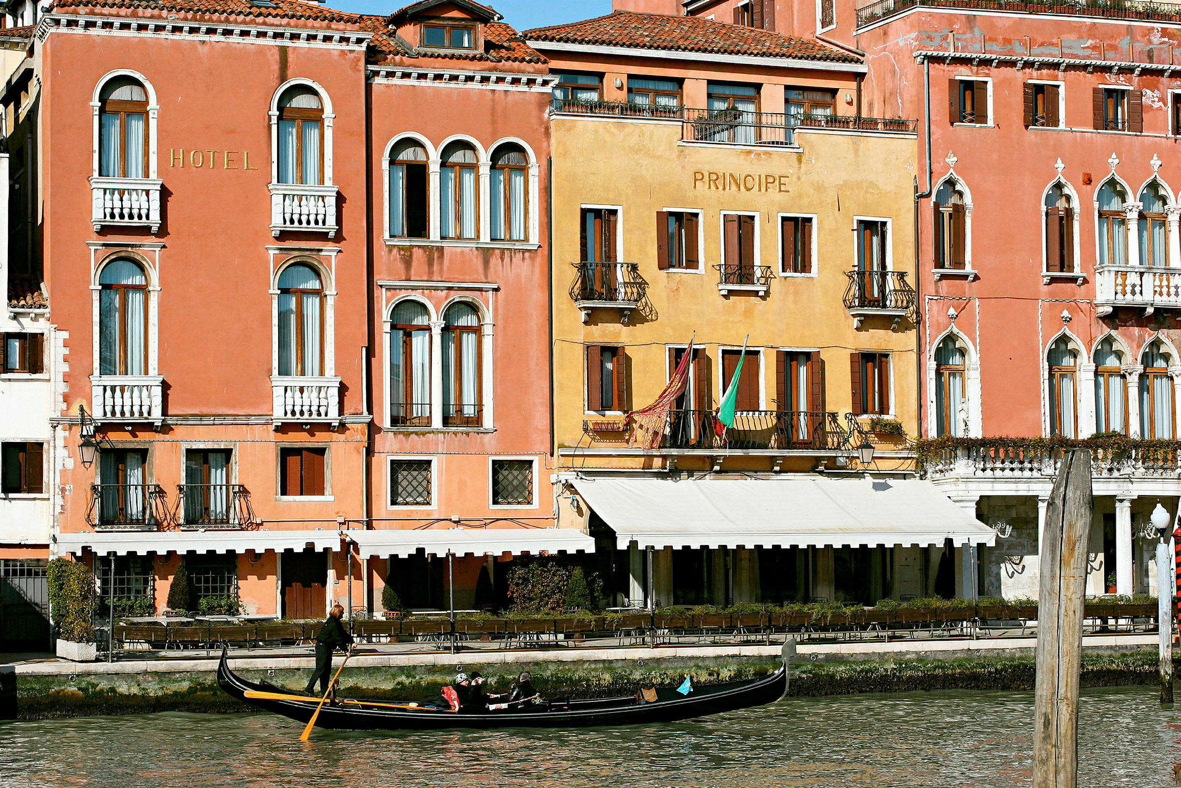 Bilde av fasadene til fargerike bygninger ved en kanal i Venezia med en gondol på vannet. (AI-generert tekst)