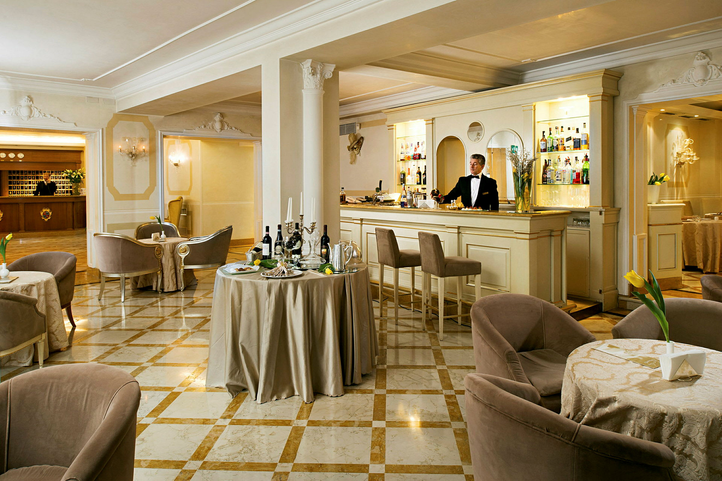 En elegant hotellbar med marmorgulv, små bord og komfortable stoler, samt en bartender ved disken. (AI-generert tekst)