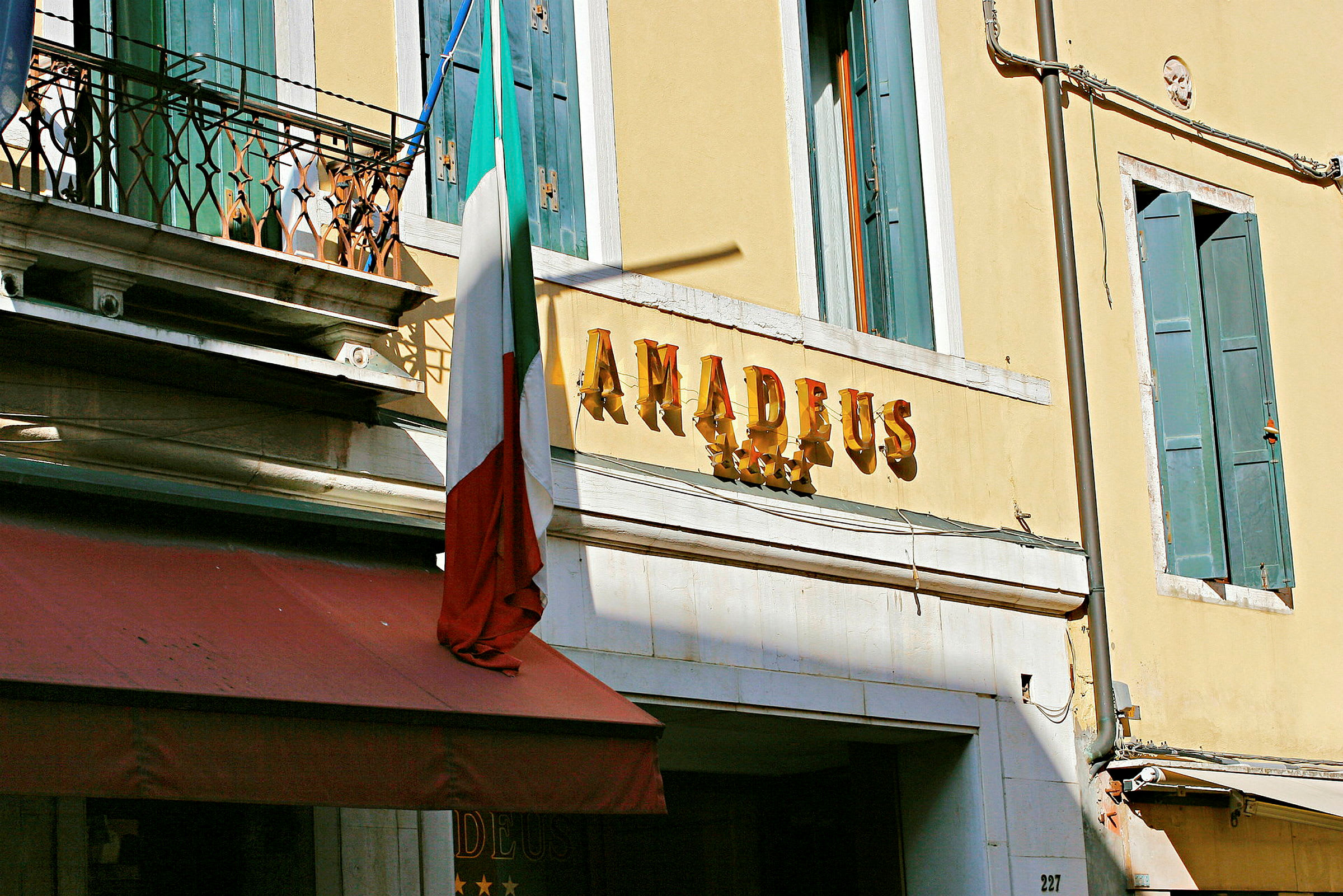 Hotellfasade med skilt som sier 'Amadeus' og et italiensk flagg. (AI-generert tekst)