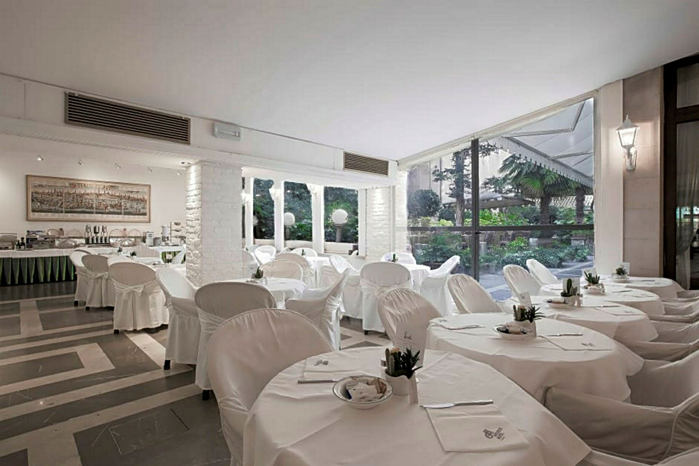 En restaurant med hvite duker og stoler, store vinduer og utsikt over en frodig hage. (AI-generert tekst)