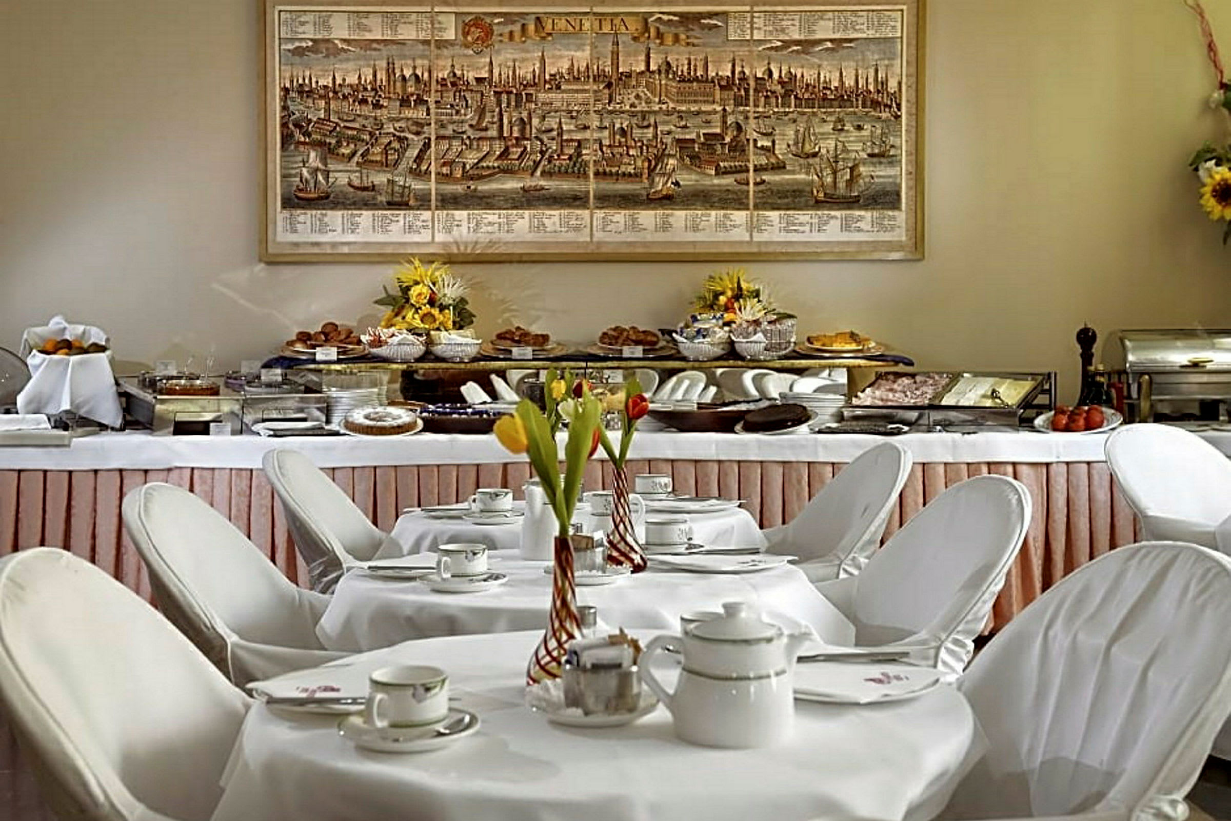 Et frokostbord dekket med porselen og blomsterdekorasjoner foran en buffé fylt med matretter. (AI-generert tekst)