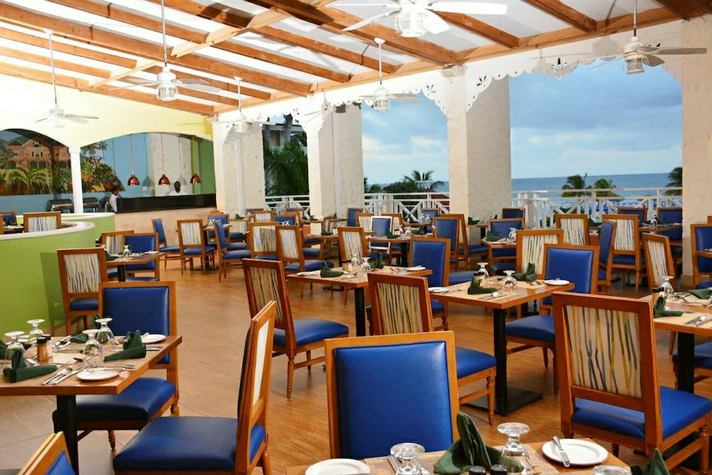 Restaurant med trebord med blå seter og dekkede bord med havutsikt. (AI-generert tekst)