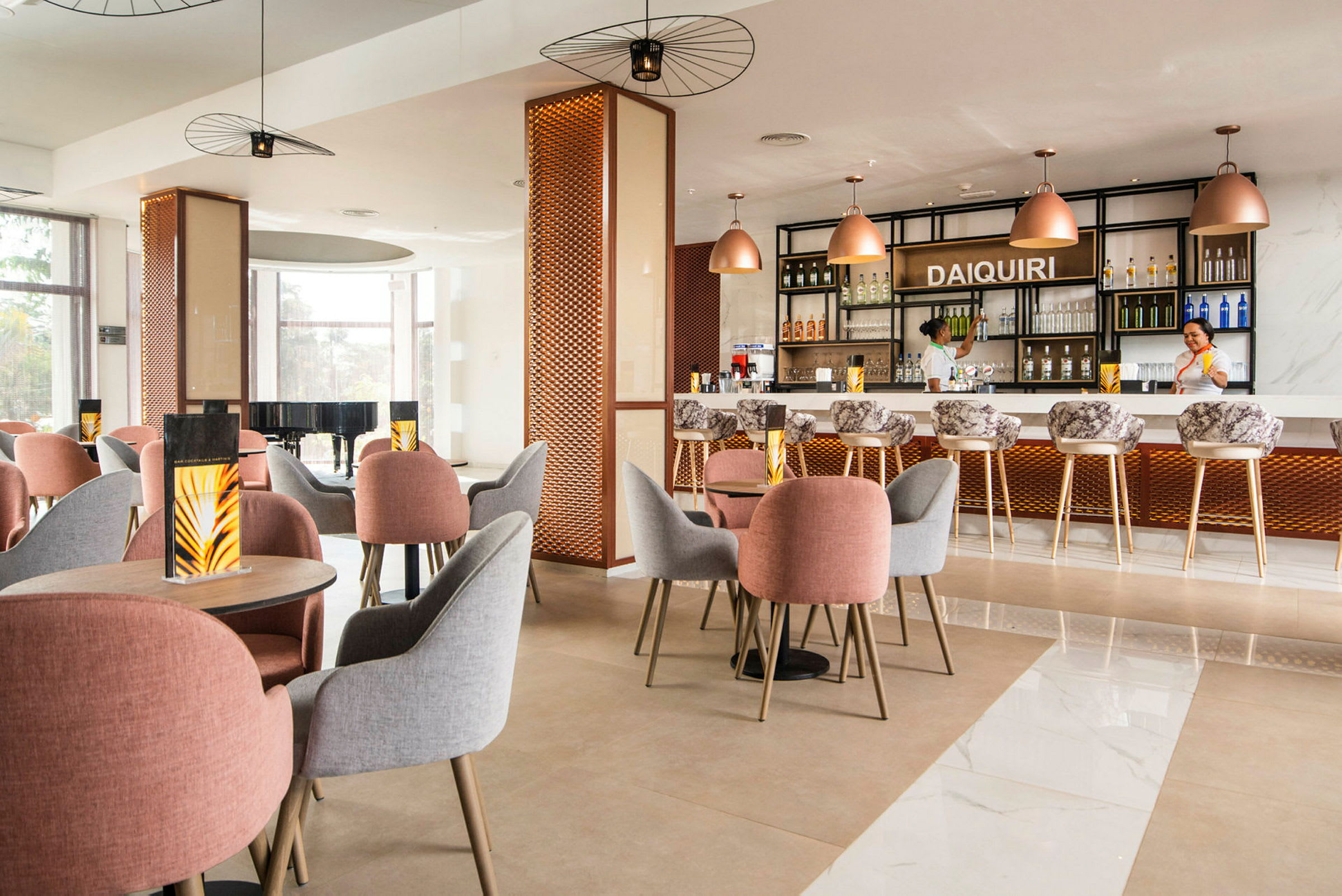 Et moderne innredet kafé eller bar med bord og stoler i forskjellige farger samt en opplyst bardisk i bakgrunnen. (AI-generert tekst)