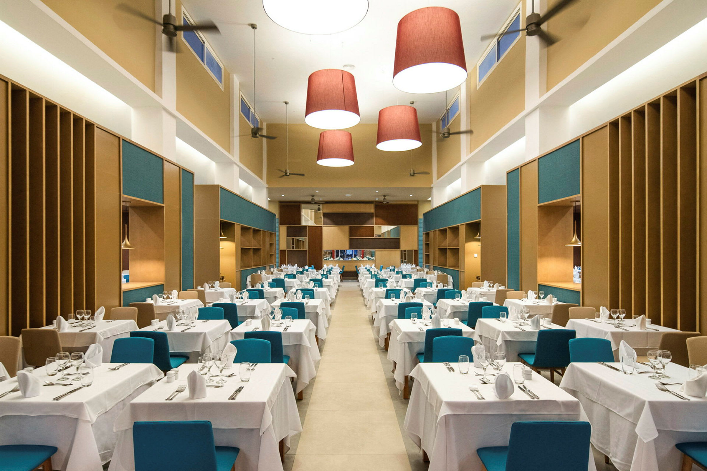 En stor og romslig restaurant med bord dekket med hvite duker og blå stoler. (AI-generert tekst)